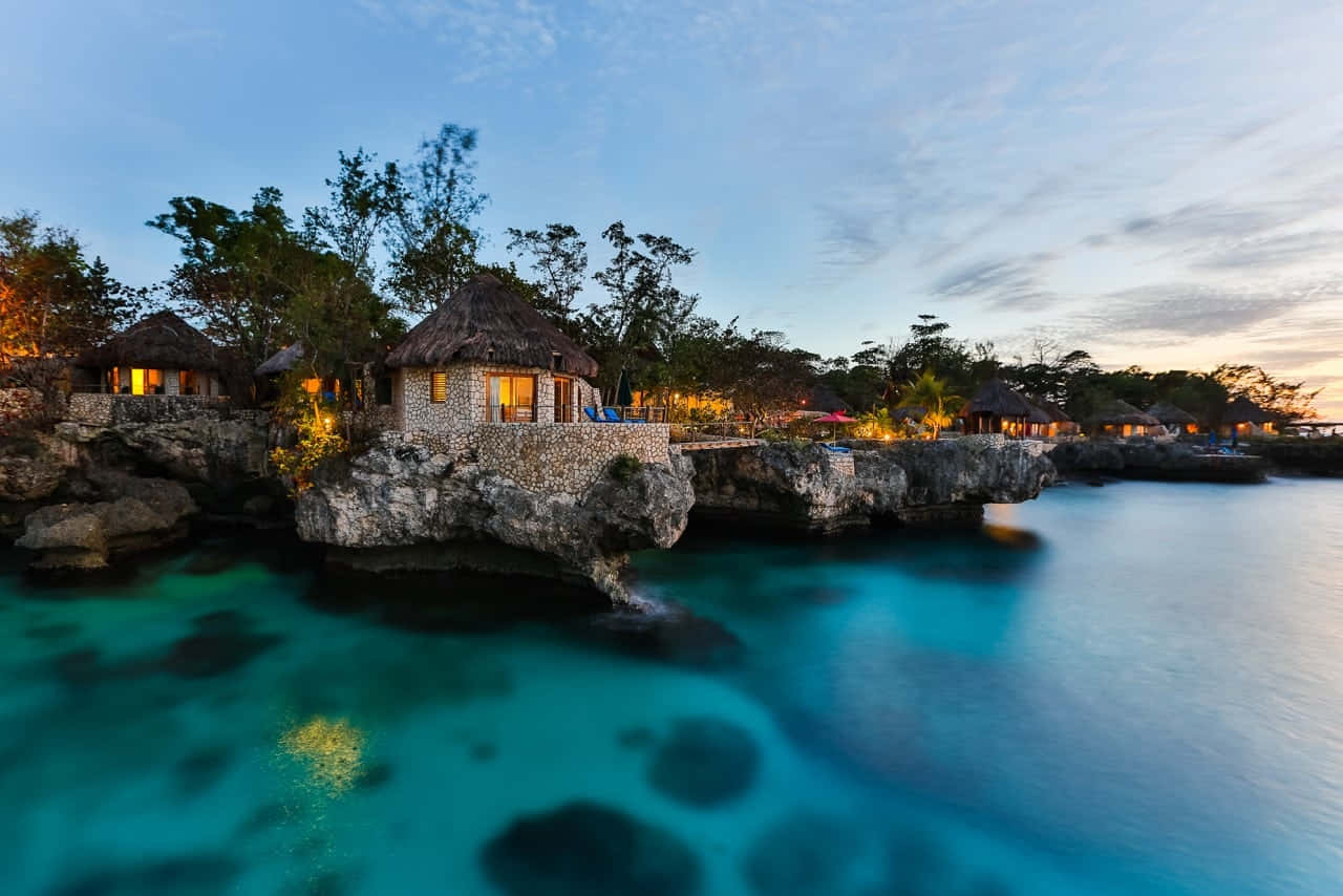 Jamaican Island 桌布 壁紙 — 珊瑚色懸崖平房在黃昏時分在碧綠海水上方溫暖地發光，天空色調柔和。