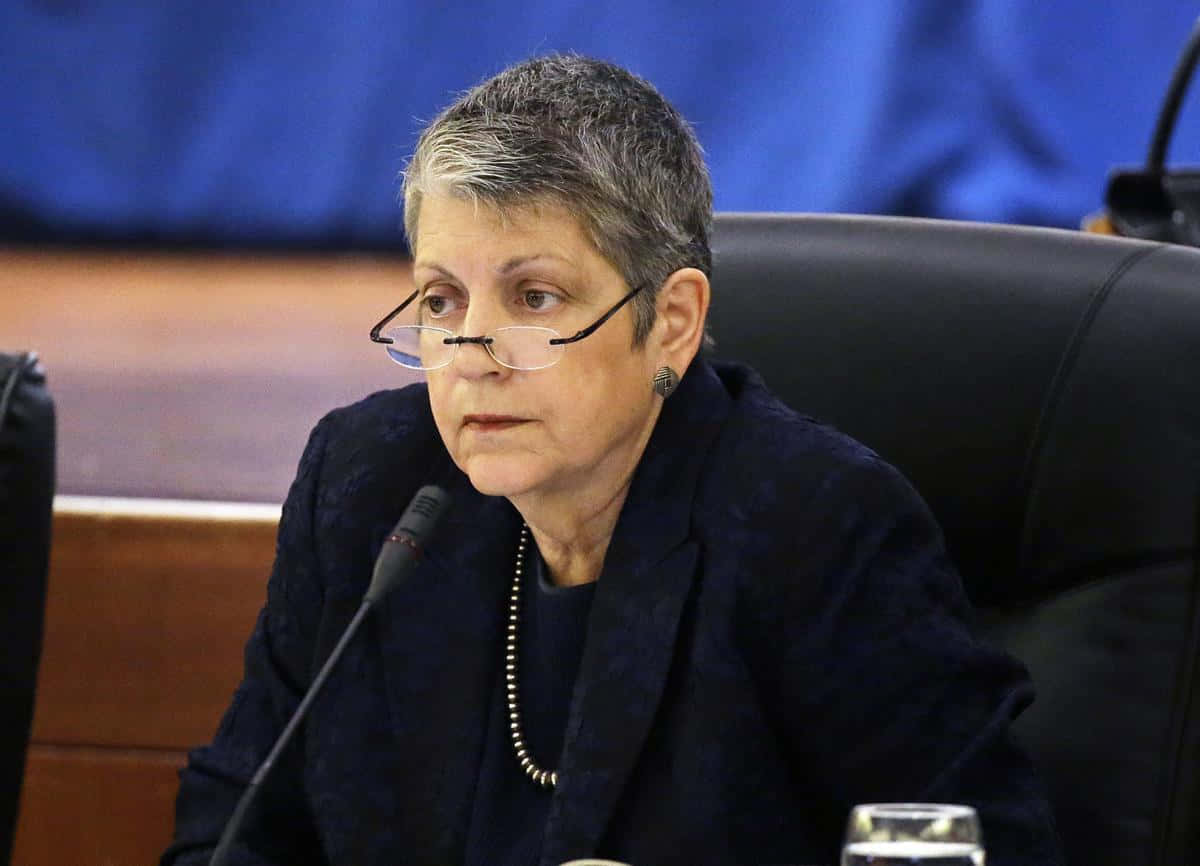 一位穿著西裝外套的女士在正式會議期間坐在有麥克風的桌子旁。