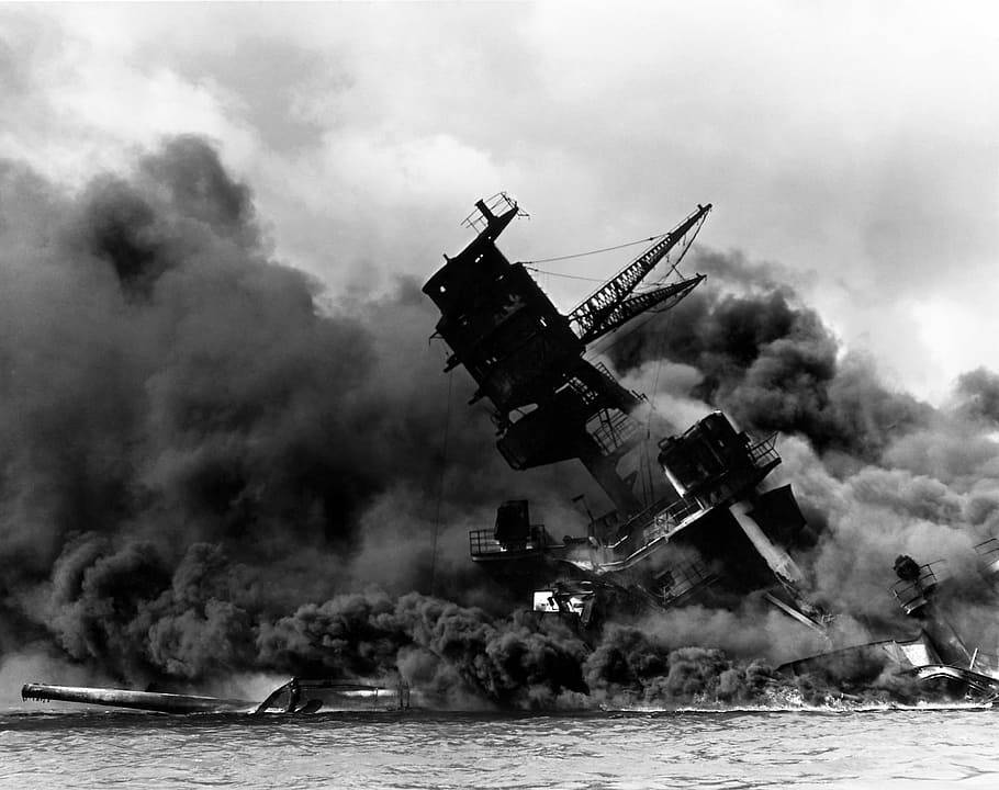 珍珠港遭轟炸沉沒的USS Arizona 壁紙 — 一艘軍艦在波濤洶湧的海域傾覆，濃煙從燃燒的殘骸中滾滾升起，天空多雲。