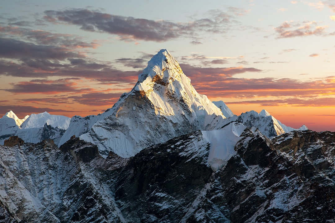 珠峰日落美景 壁紙 — 白雪覆蓋的山峰在日出時閃耀著金色光芒，映襯著帶有散雲的火橙色和粉紅色天空。