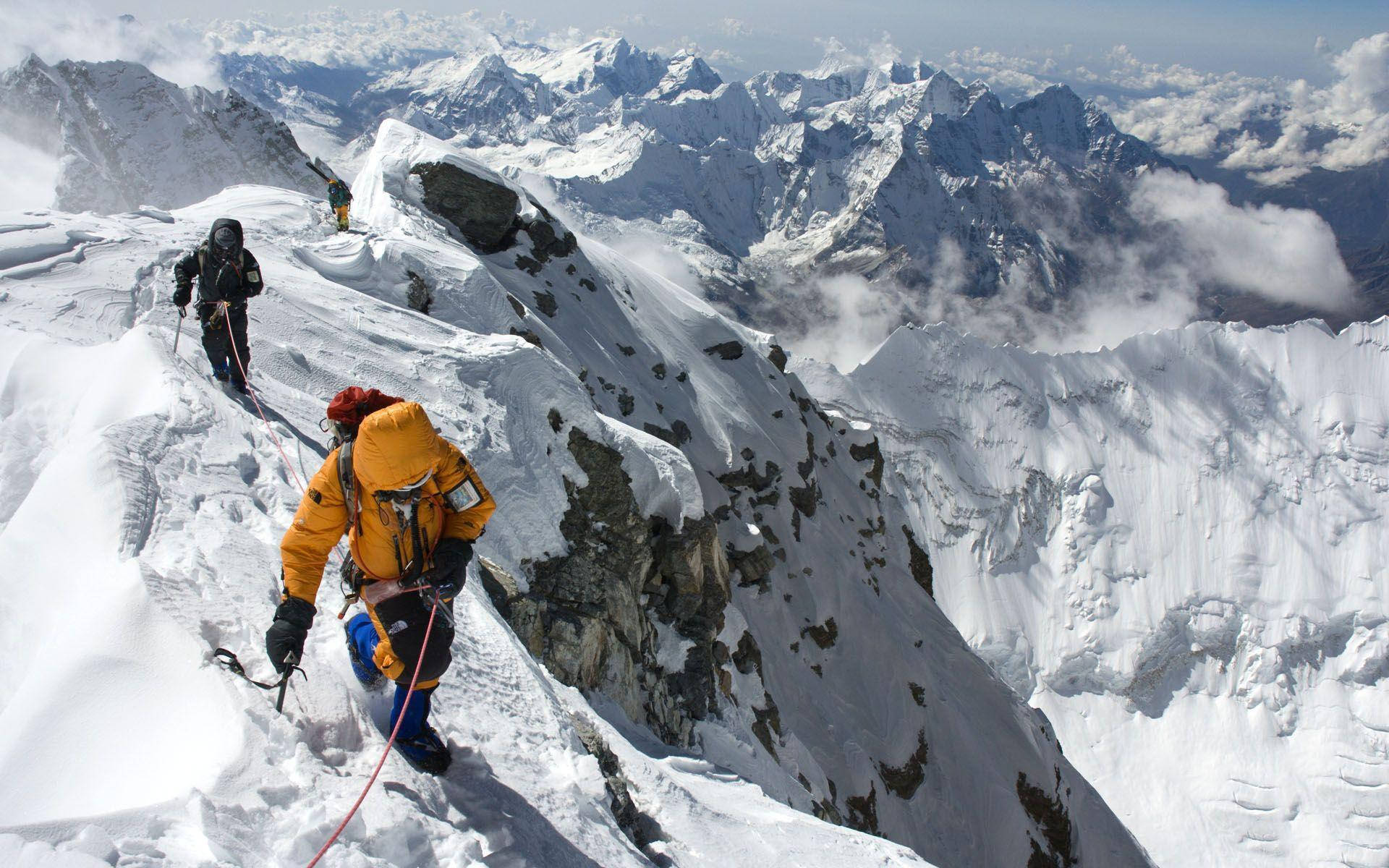 登山者在戲劇性的阿爾卑斯山背景下攀登積雪山脊。