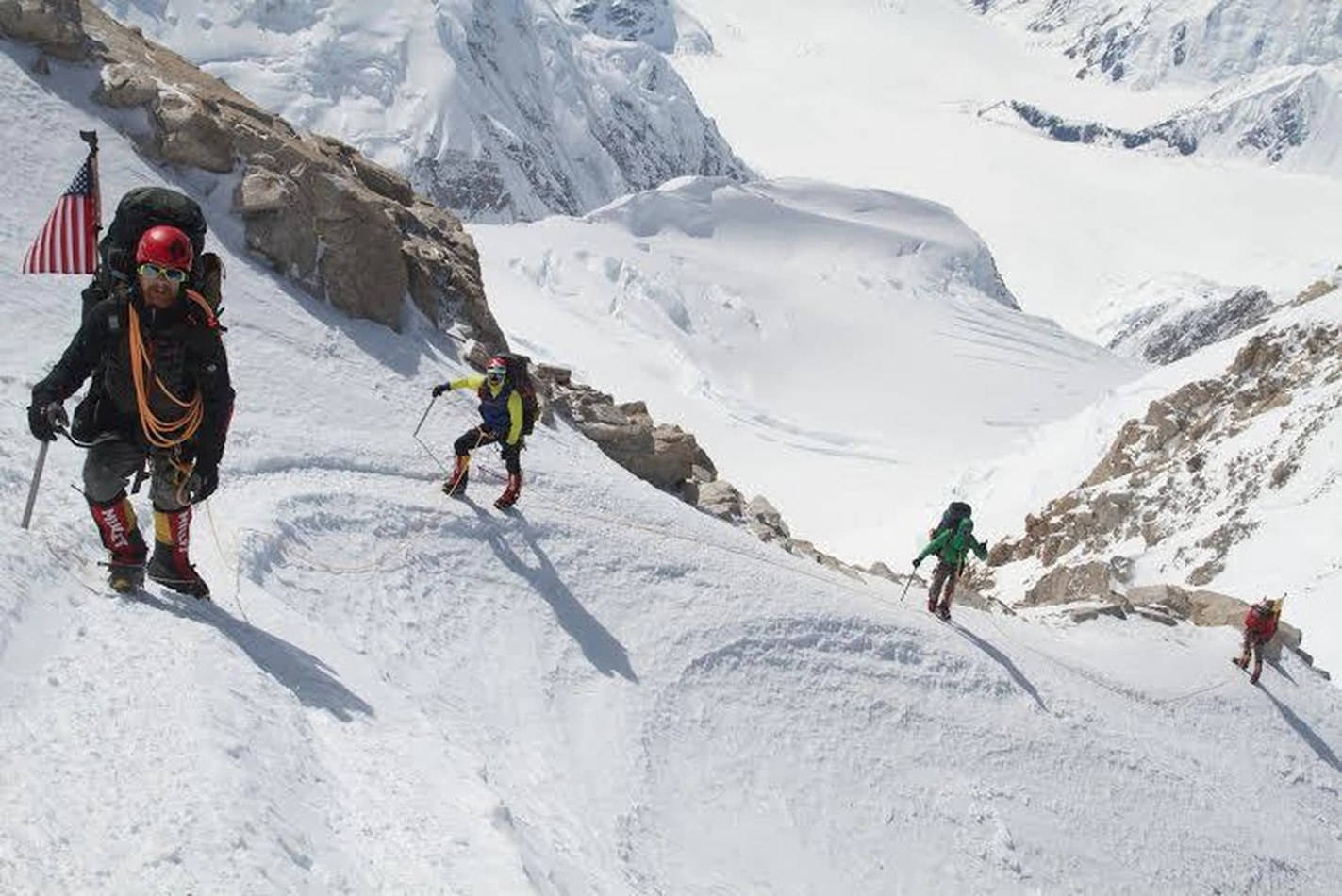 四位登山者用冰斧和繩索攀登雪山斜坡。