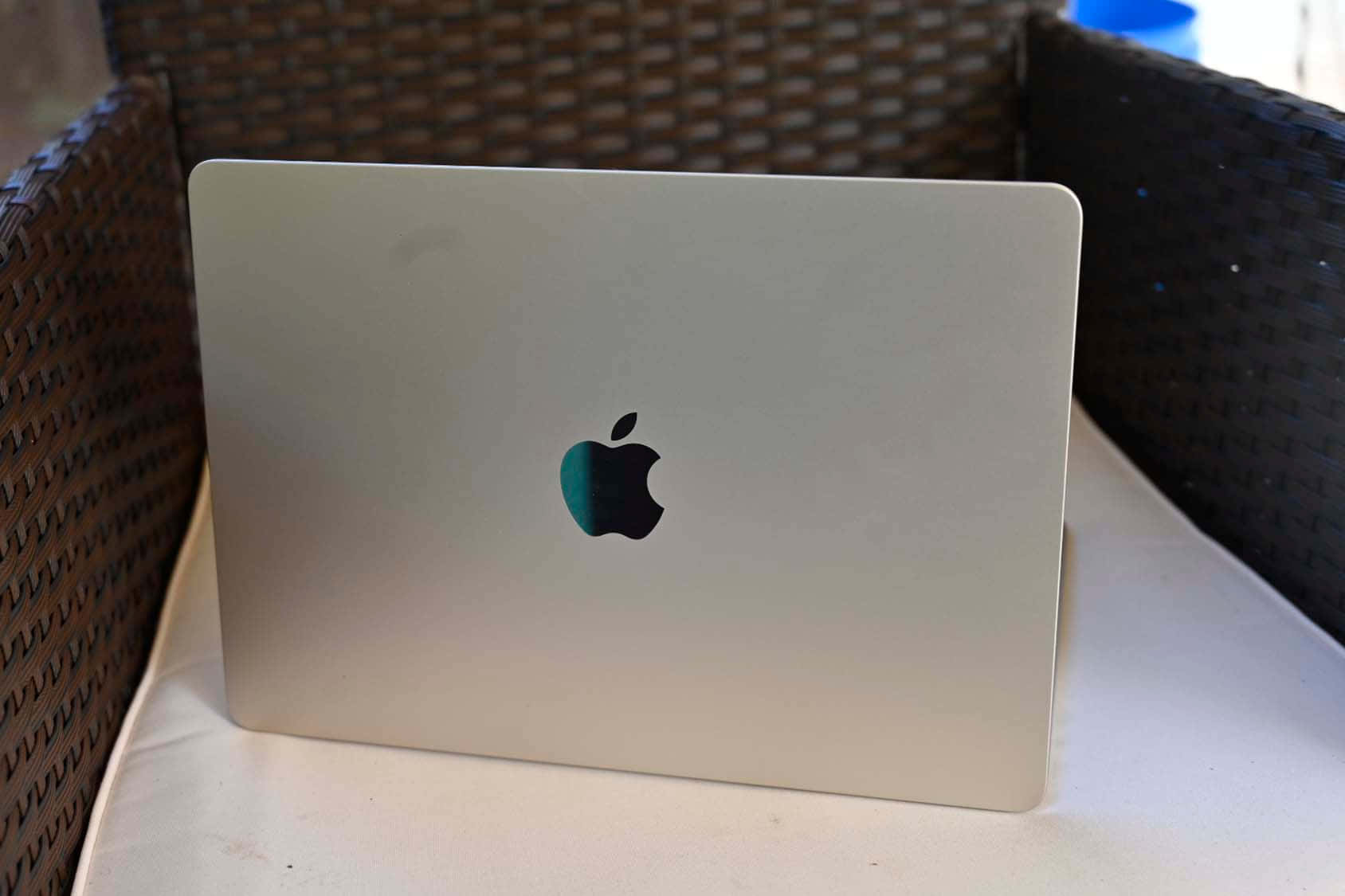 現代 MacBook Pro，隨時準備工作 壁紙 — 銀色MacBook蓋上帶有Apple標誌，放在戶外白色軟墊柳條椅上。
