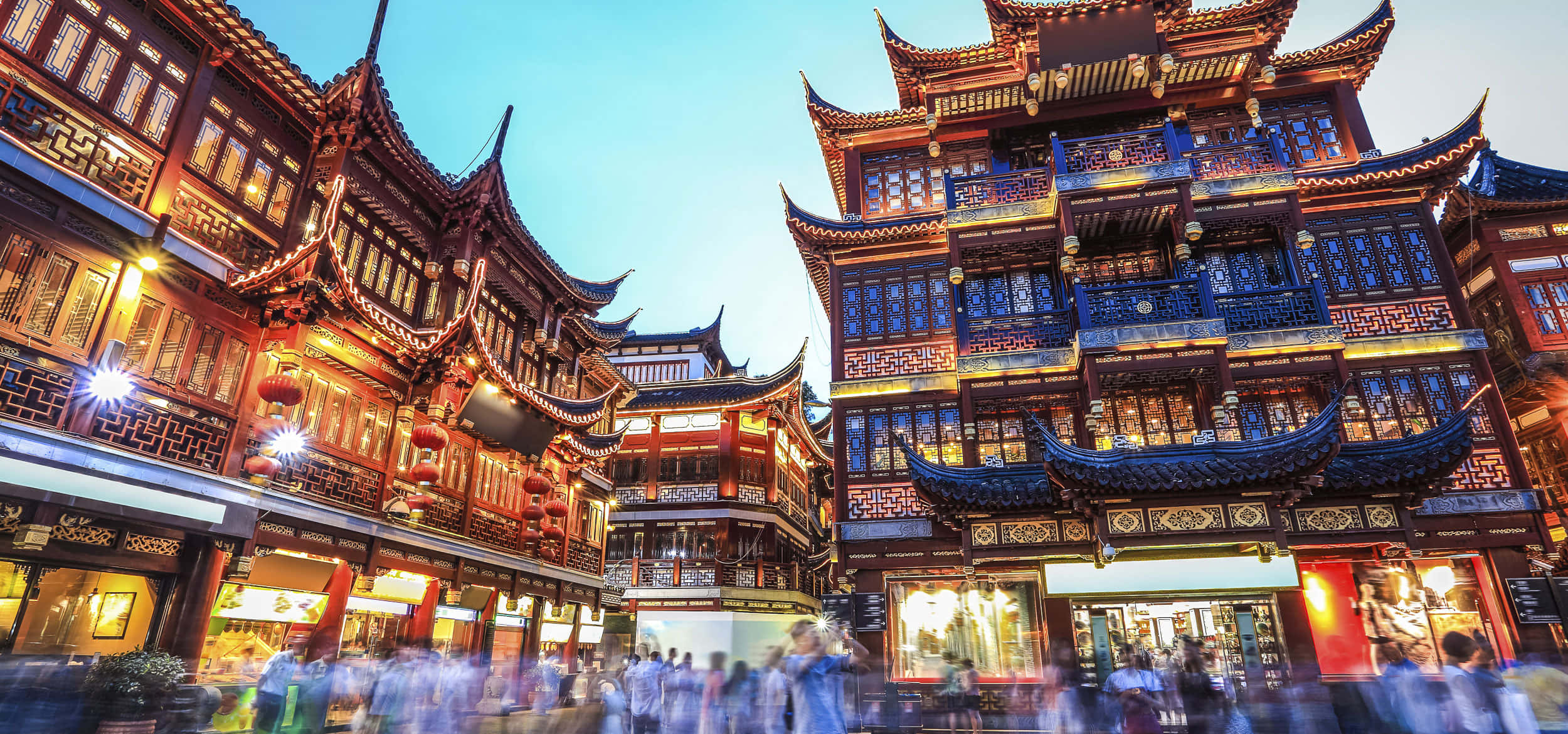 現代中國之美 壁紙 — 傳統中式建築在暮色天空下溫暖地發光，模糊的人群在繁華的歷史街道上移動。