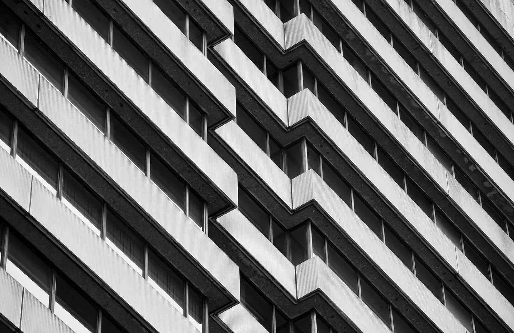 Black And White Architecture 桌布 壁紙 — 現代主義建築幾何外牆的黑白特寫，帶有重複的窗戶圖案。