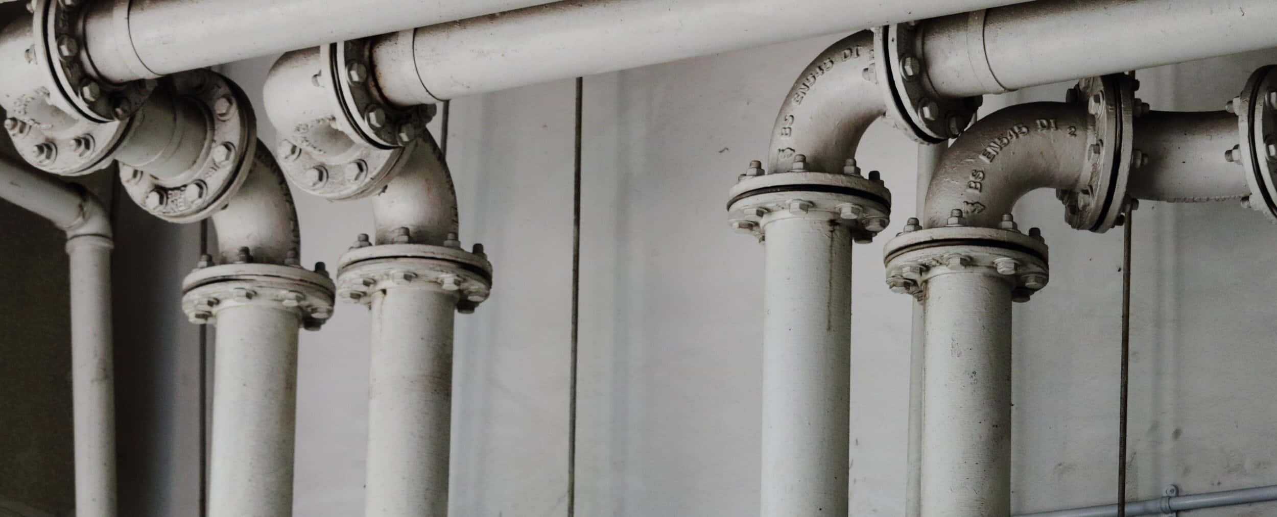 現代住宅 Plumbing 系統 壁紙 — 特寫風化白色工業管道，帶有螺栓法蘭，靠著素色牆壁。