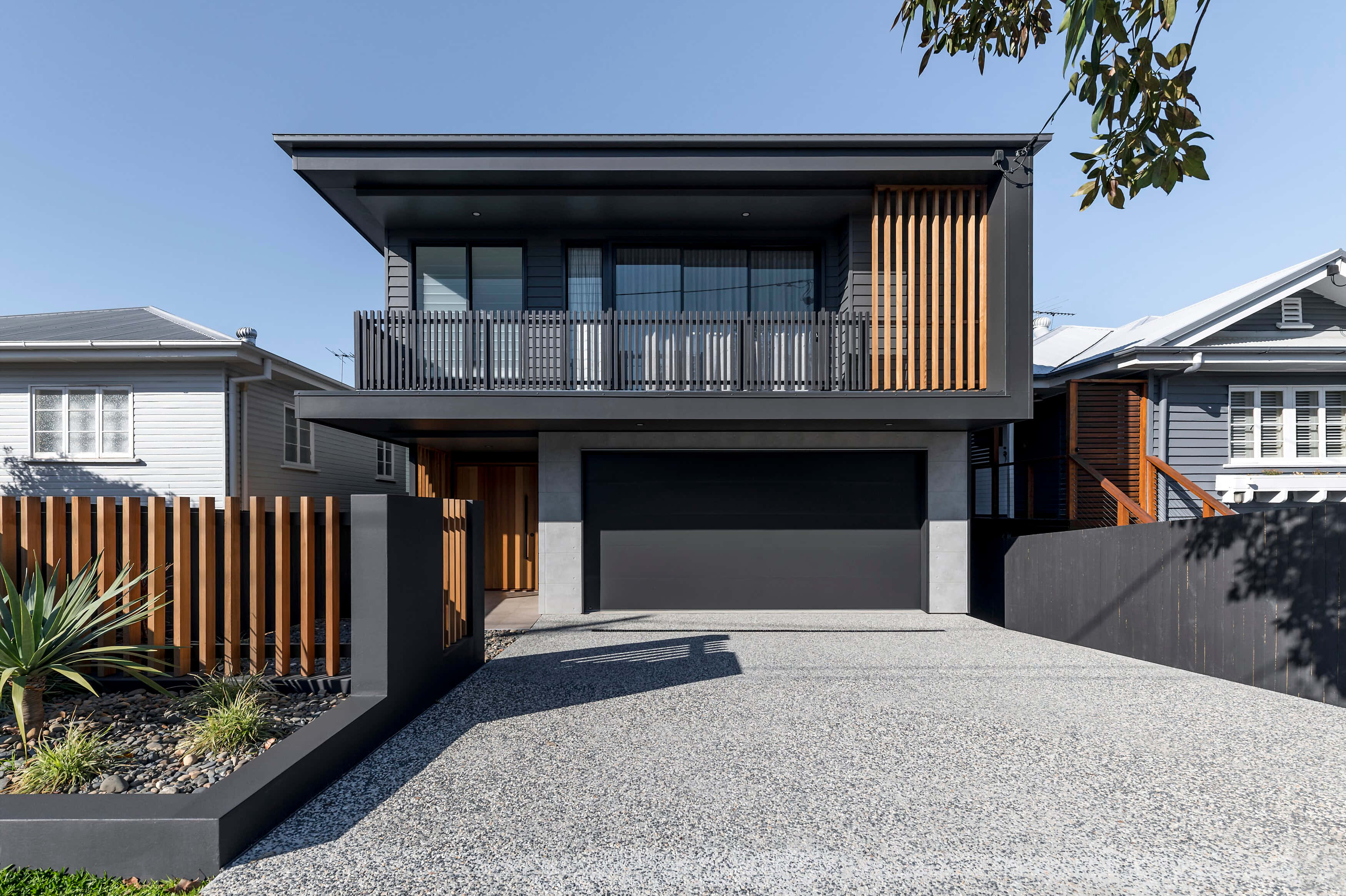 Big House 桌布 壁紙 — 現代兩層住宅，深灰色外牆配木條裝飾，碎石車道，藍天白雲下。