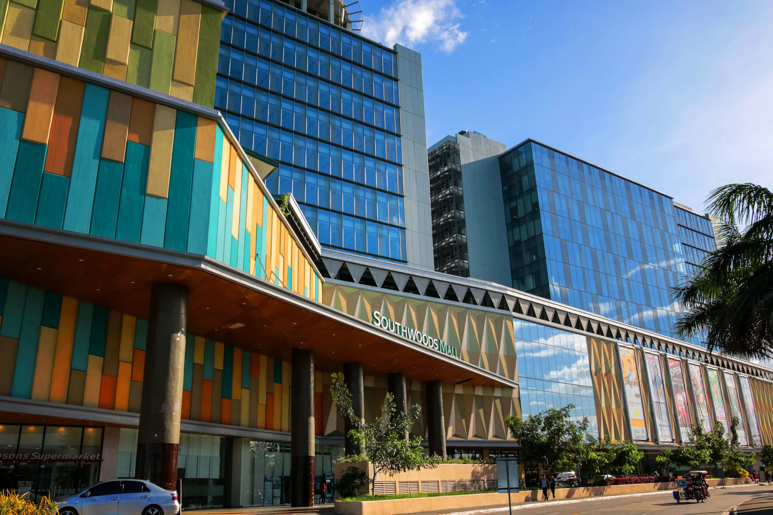 Mall 桌布 壁紙 — 現代嘅Southwoods Mall喺晴朗藍天、棕櫚樹同汽車附近，展現出充滿活力嘅彩色面板同玻璃外牆。