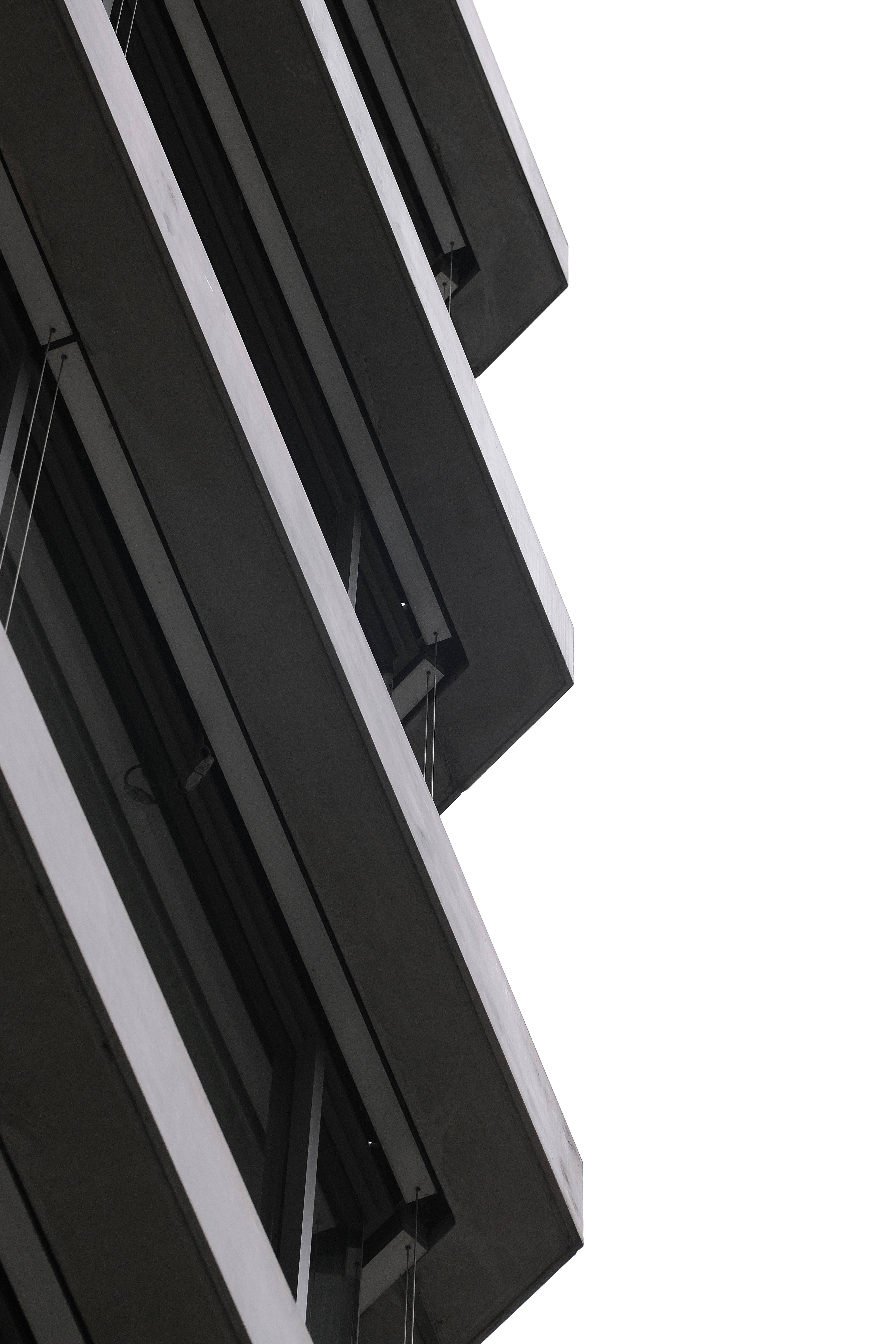 現代外牆暗調 4K 壁紙 — 一座簡約現代建築的外牆，以大膽的黑白幾何線條向上傾斜，映襯著明亮的白色天空。