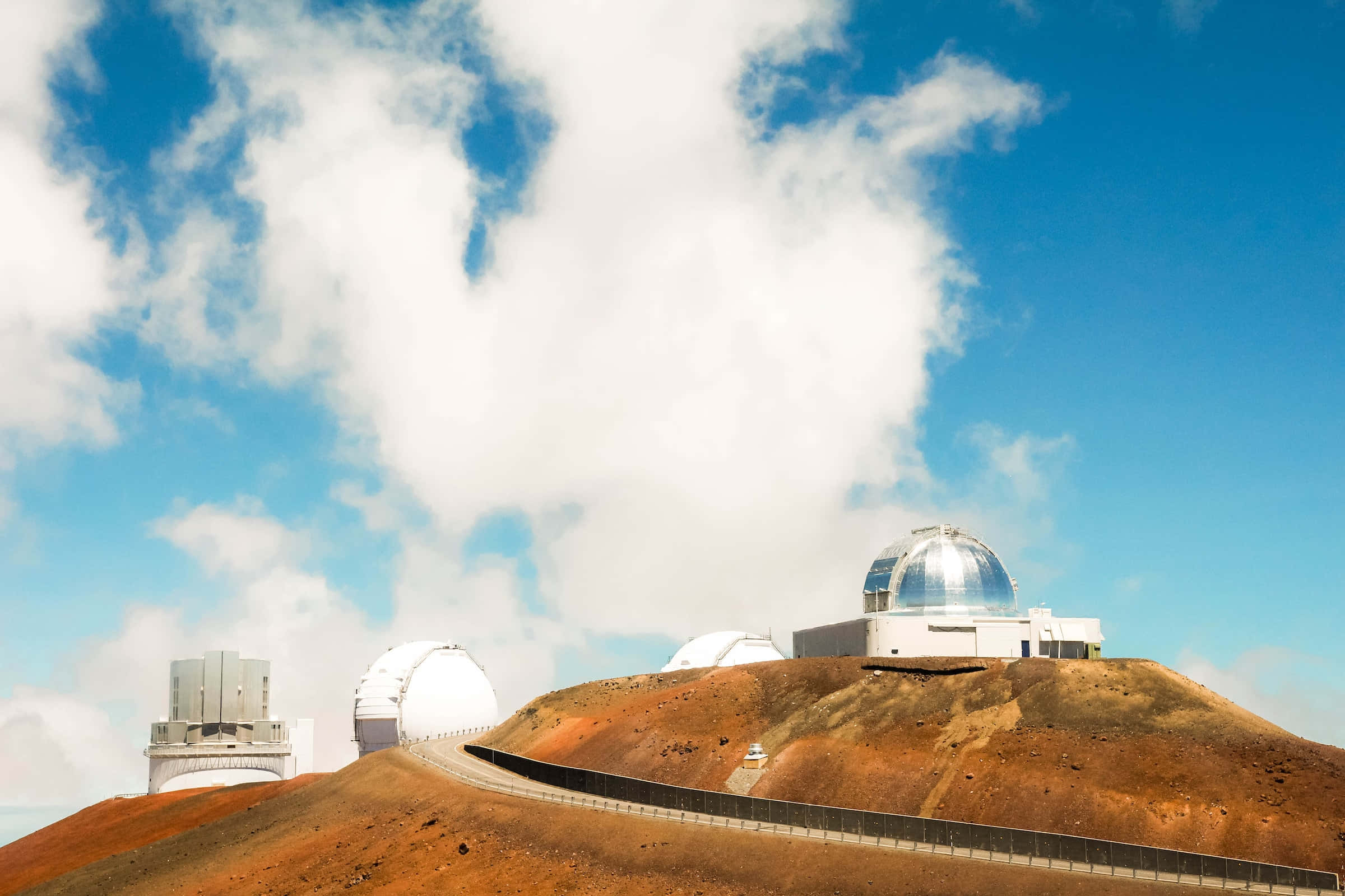Space Observation 桌布 壁紙 — 現代天文台配備圓頂望遠鏡，坐落於崎嶇的紅褐色山丘上，上方是明亮的藍天和蓬鬆的白雲。