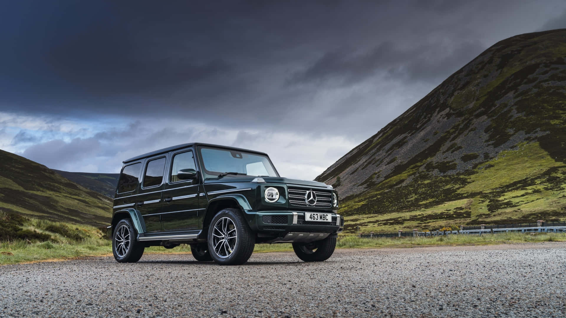 深綠色平治 G-Class SUV 停泊在山區碎石路上，天空風暴密佈。