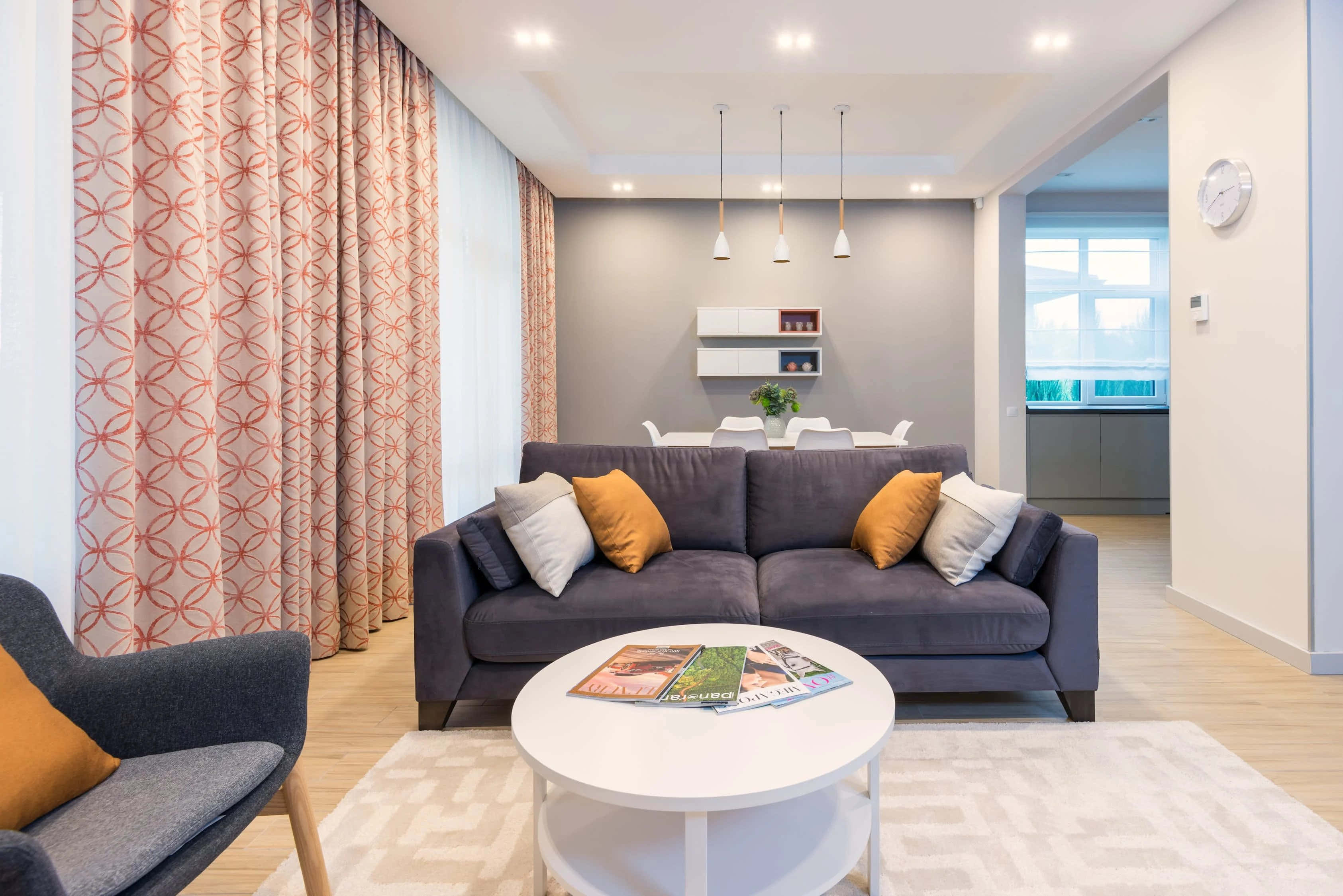 Apartment 桌布 壁紙 — 現代客廳，配有灰色梳化、橙色枕頭、圖案窗簾和白色茶几，上方有明亮的吊燈。