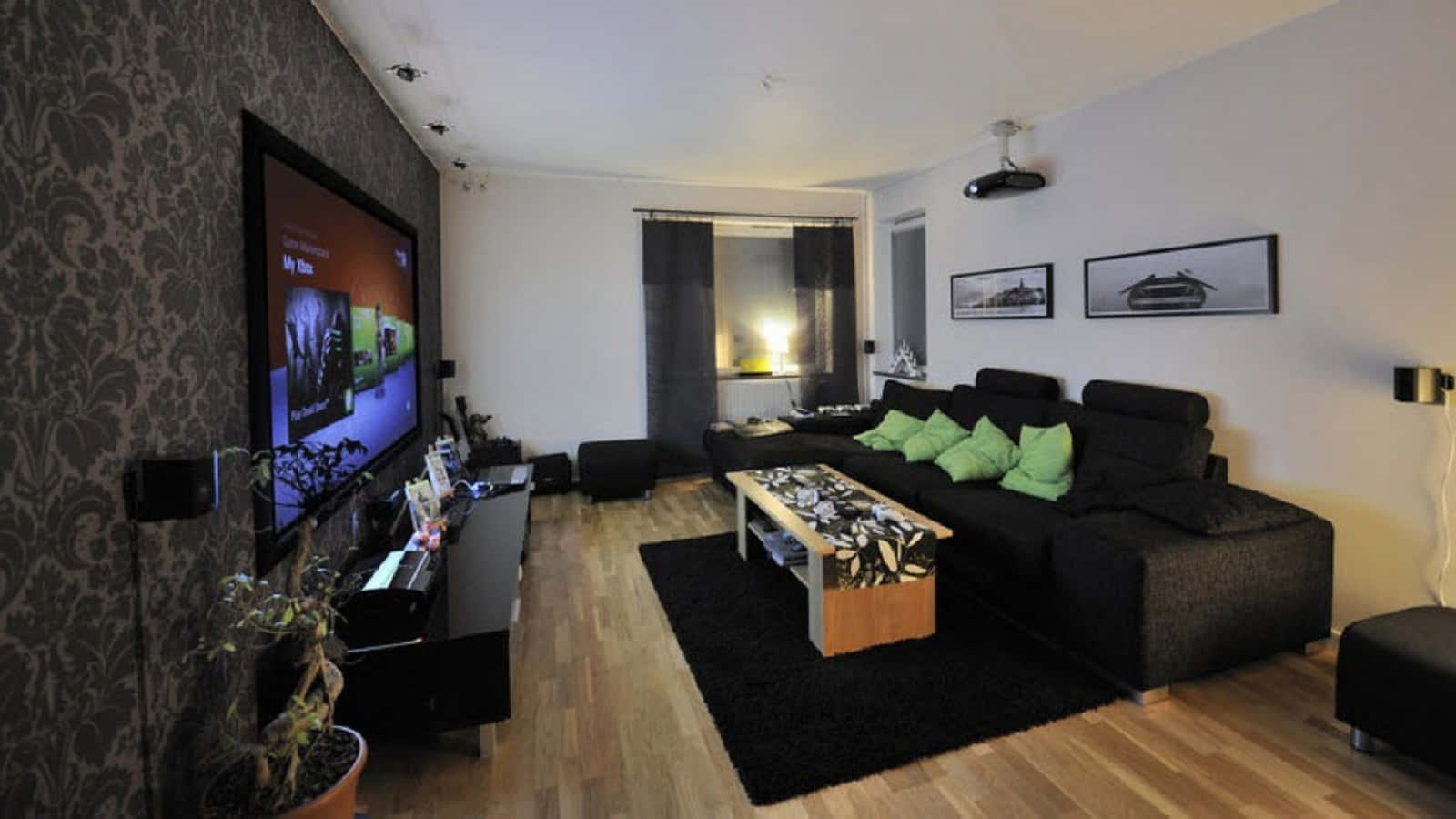 Home Cinema 桌布 壁紙 — 現代客廳，配有黑色沙發、綠色靠墊、木地板和安裝在圖案壁紙牆上的大電視。