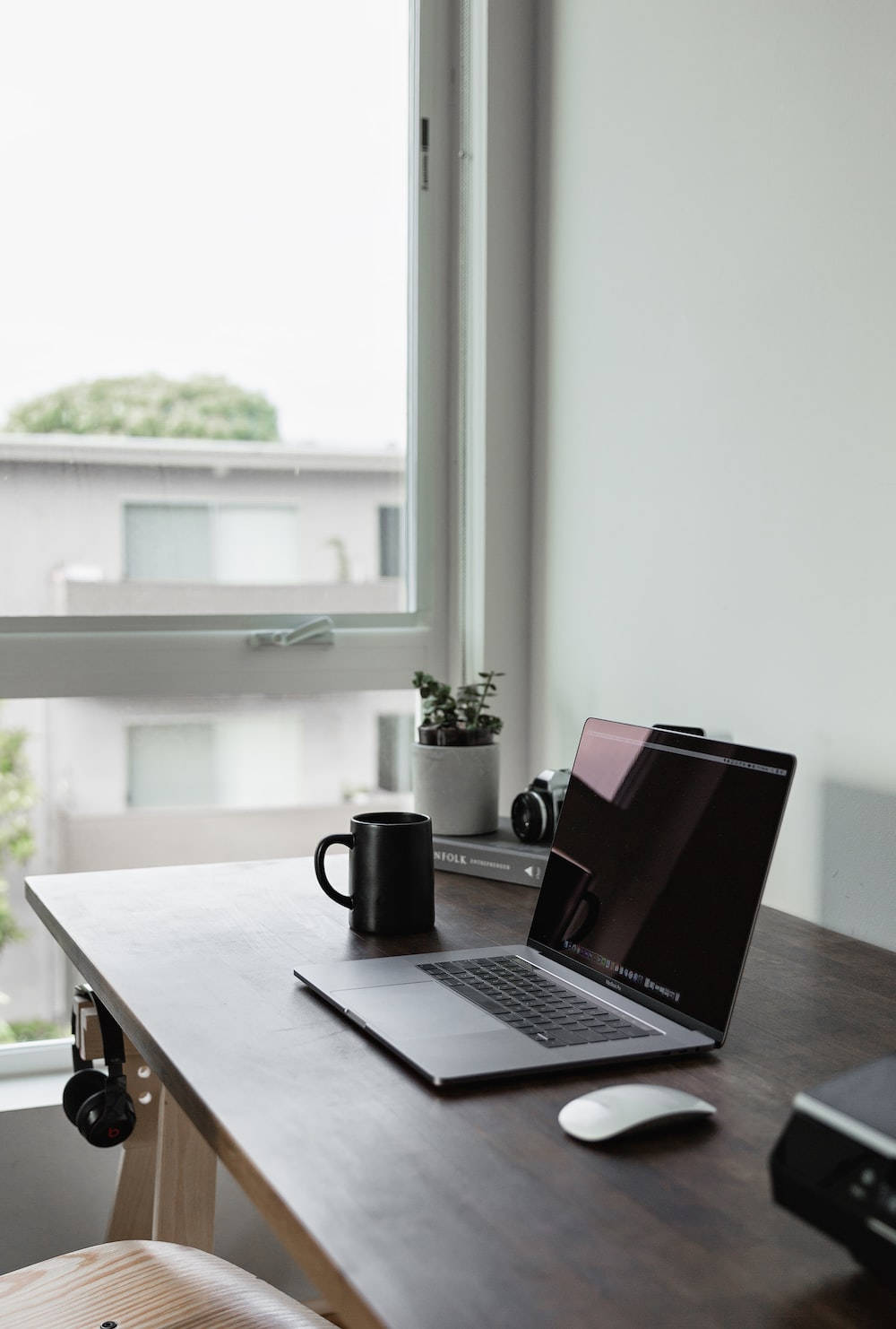 Best Laptop 桌布 壁紙 — 現代家居辦公室的明亮窗邊，一張簡約木桌上放著手提電腦、馬克杯、耳機和小盆栽。