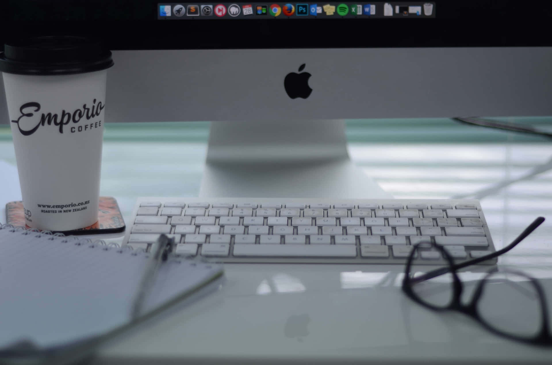 一張整潔的桌子，配有咖啡、鍵盤、眼鏡和 Apple iMac，適合工作或學習。