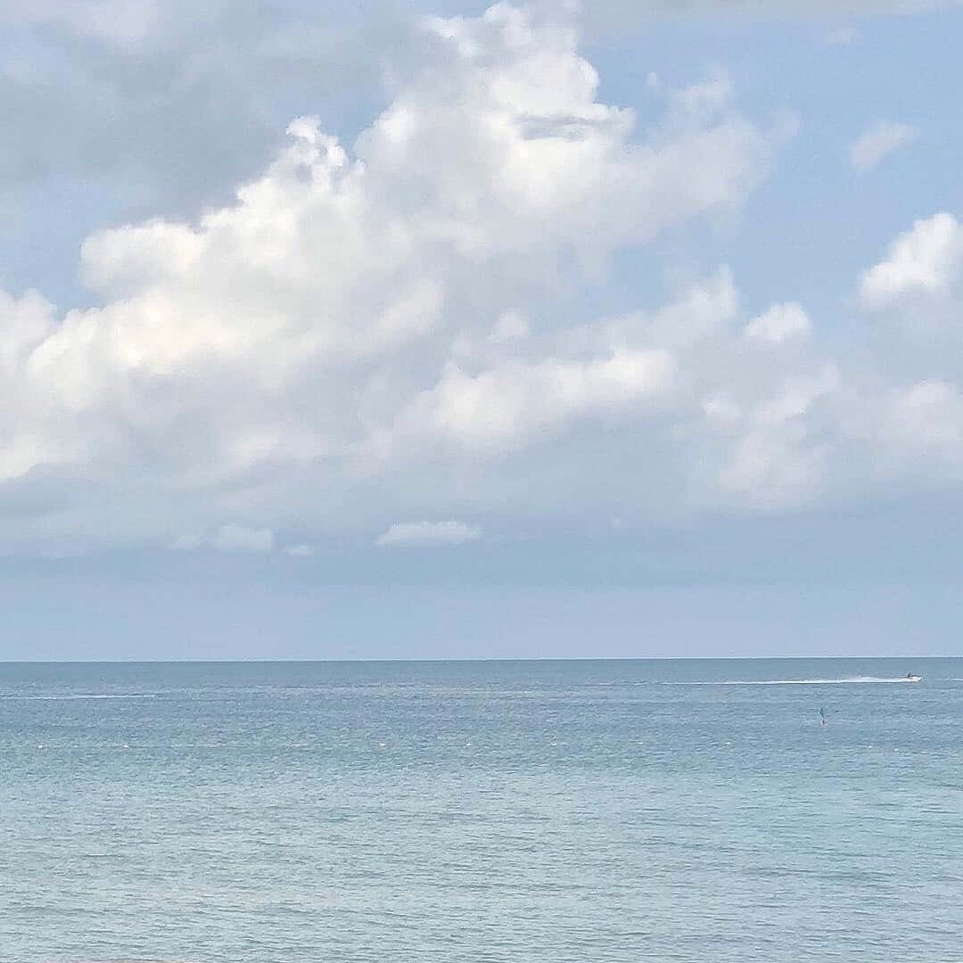 現代對藍色之美與寧靜的致敬 壁紙 — 寧靜的海洋在廣闊的天空下延伸，天空佈滿蓬鬆的白雲，一艘小船在平靜的碧綠海水上留下一道航跡。