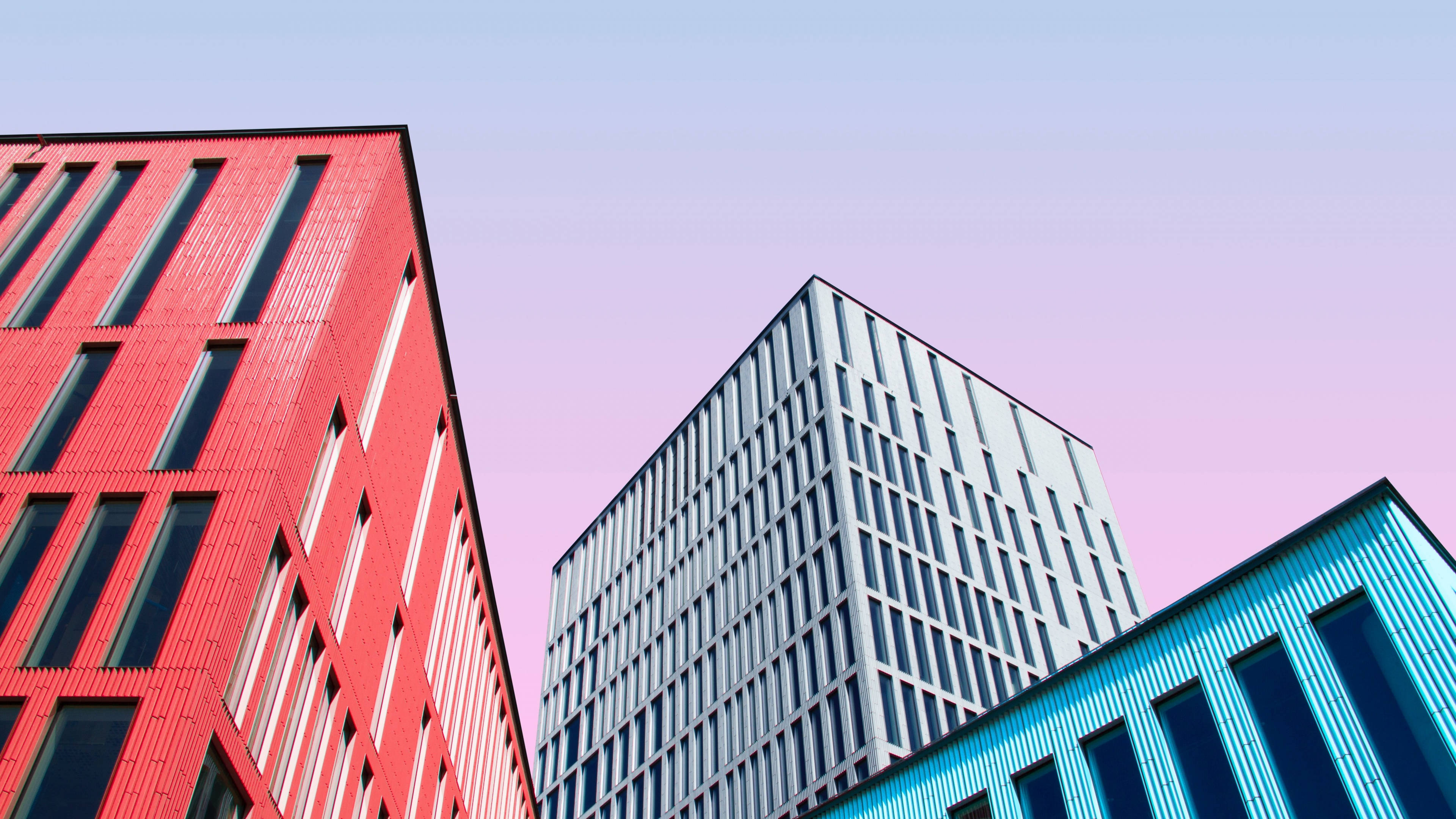 Buildings 桌布 壁紙 — 現代建築以鮮明的紅、藍、灰色調，在柔和的粉紅與薰衣草色天空映襯下矗立。