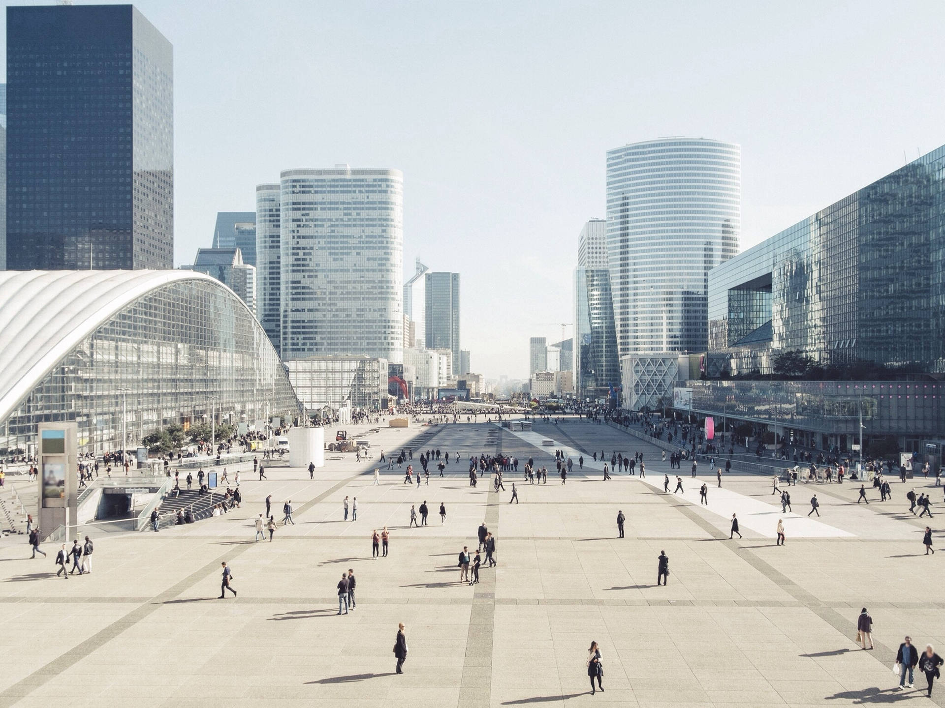 人群在寬敞的城市廣場上漫步，四周環繞著高聳的玻璃和鋼鐵建築。