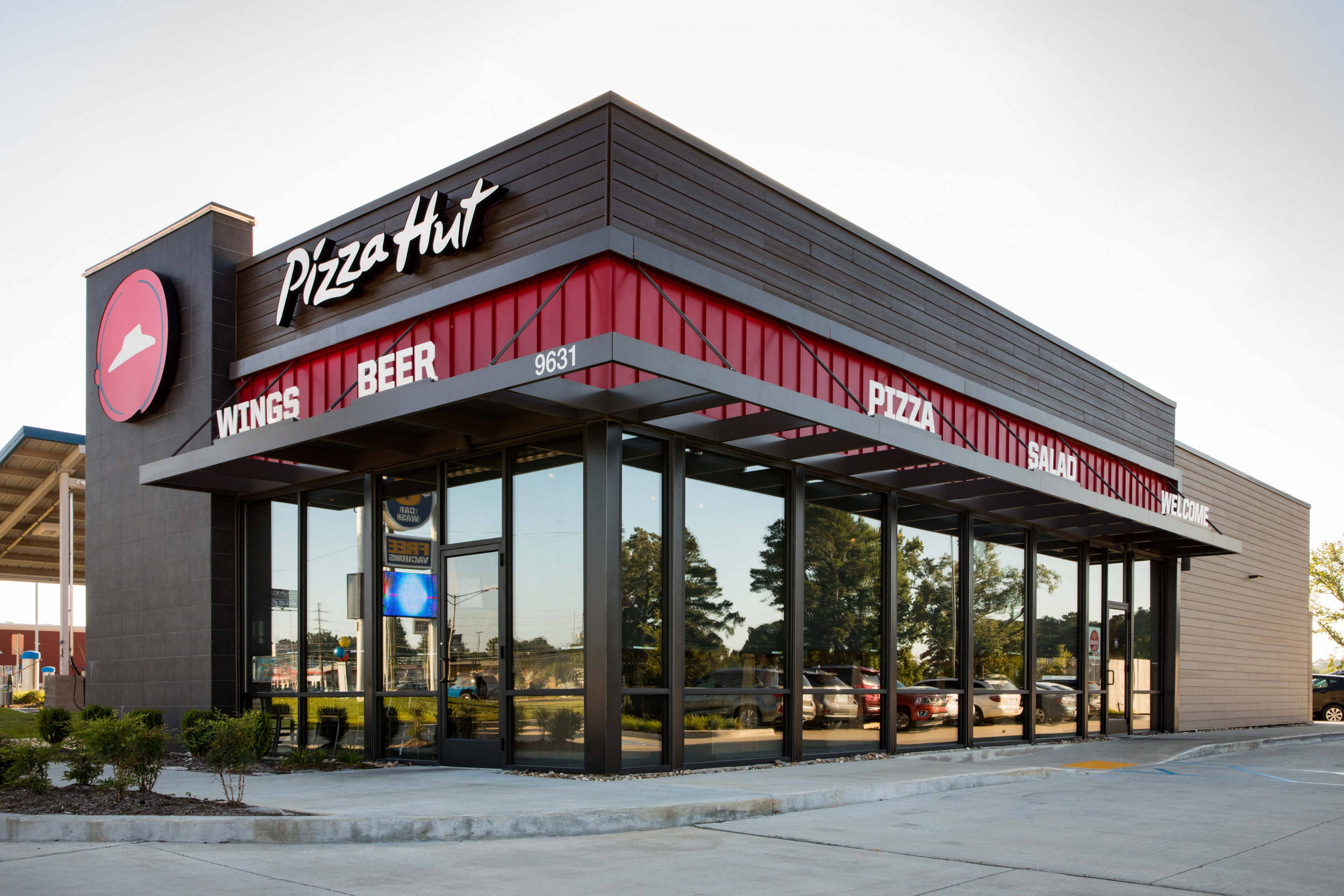 現代必勝客餐廳 壁紙 — 現代Pizza Hut餐廳，擁有醒目紅黑外牆、大型玻璃窗，黃昏時外面停有車輛。