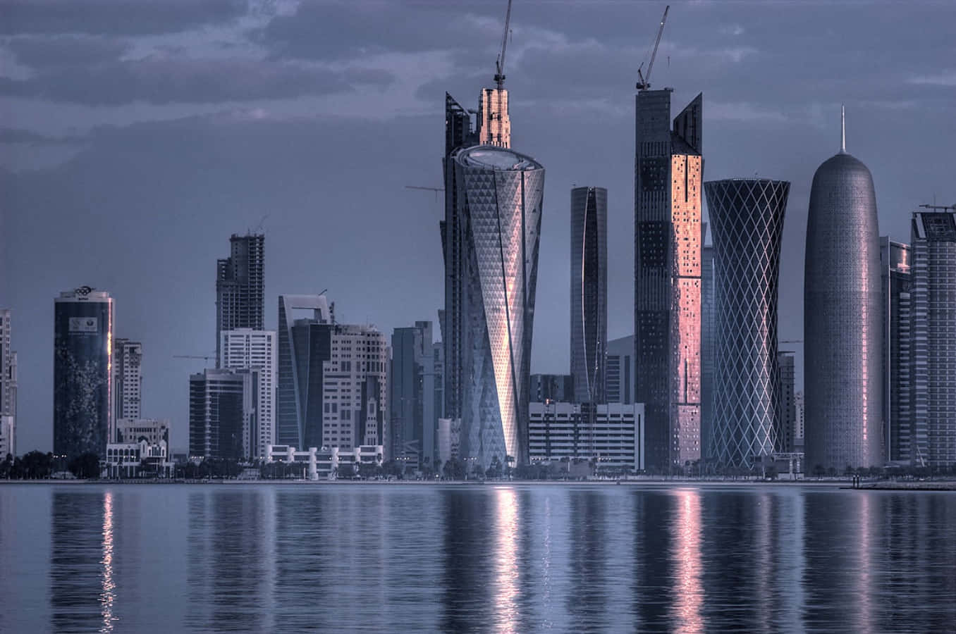 Qatar 桌布 壁紙 — 現代摩天大樓以獨特的幾何設計在昏暗天空下的平靜水面上倒映。