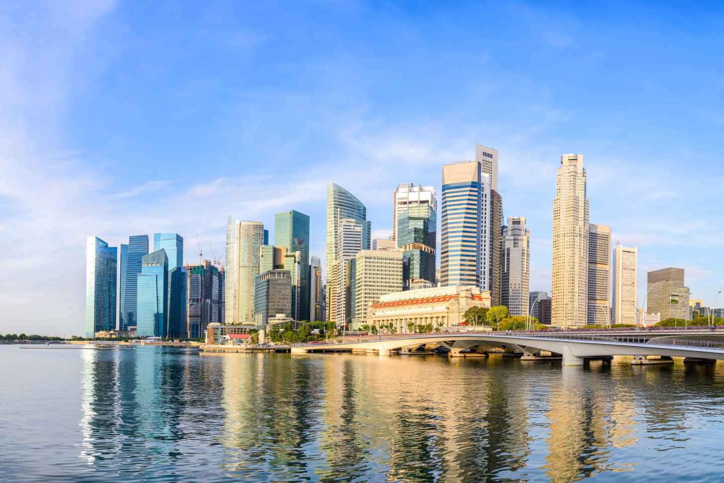 Singapore 桌布 壁紙 — 現代摩天大樓在平靜的水面上倒映，藍天白雲下，前景有一座橋樑橫跨。