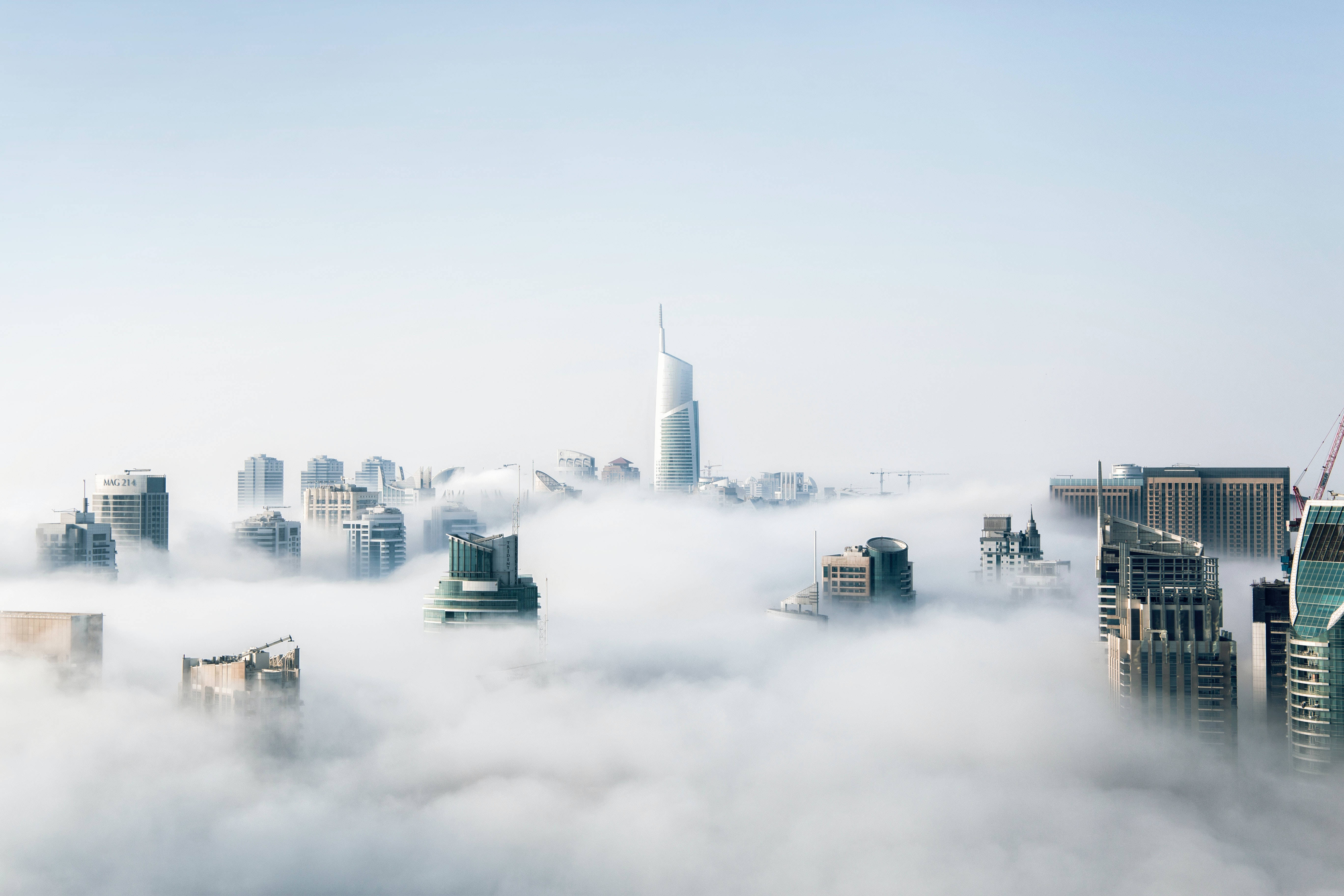 雲 桌布 壁紙 — 現代摩天大樓在淡藍色天空下從厚厚的霧毯中浮現。