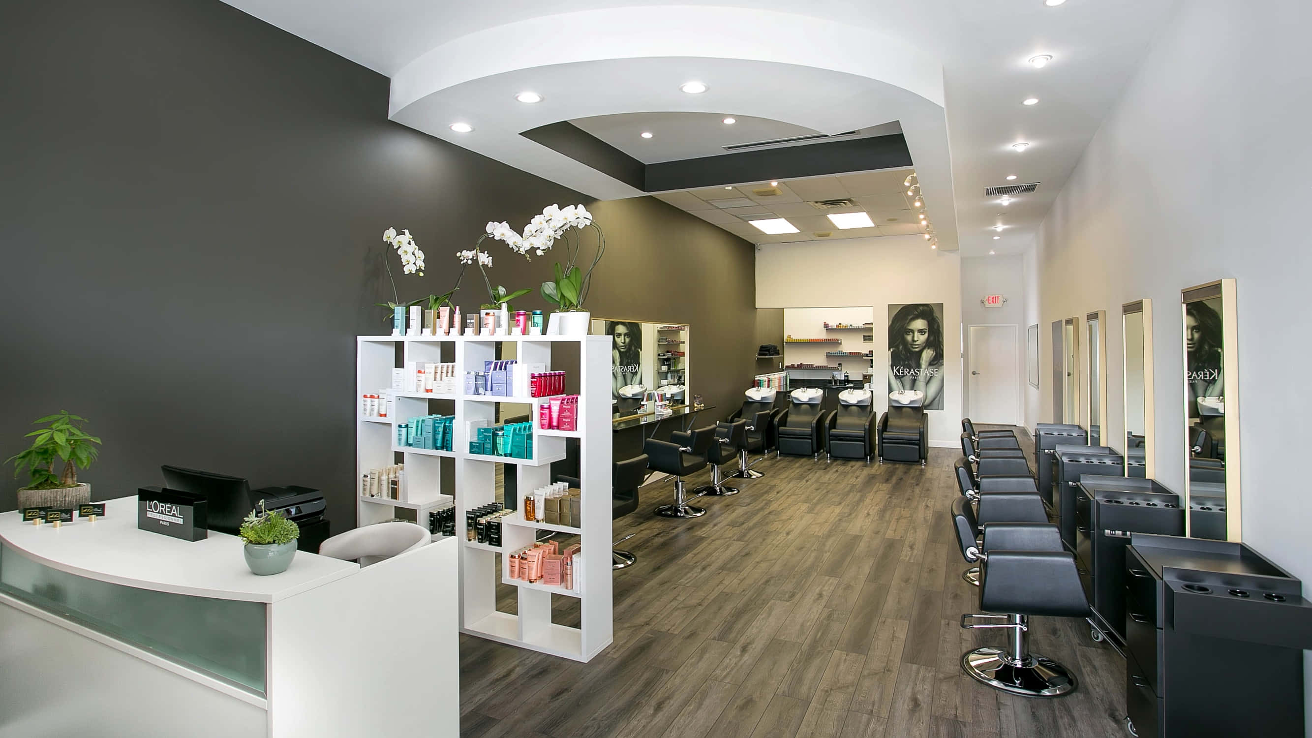 Hair Salon 桌布 壁紙 — 現代時尚髮廊，配有黑色椅子、白色架子、木地板，上方有明亮的吊燈。