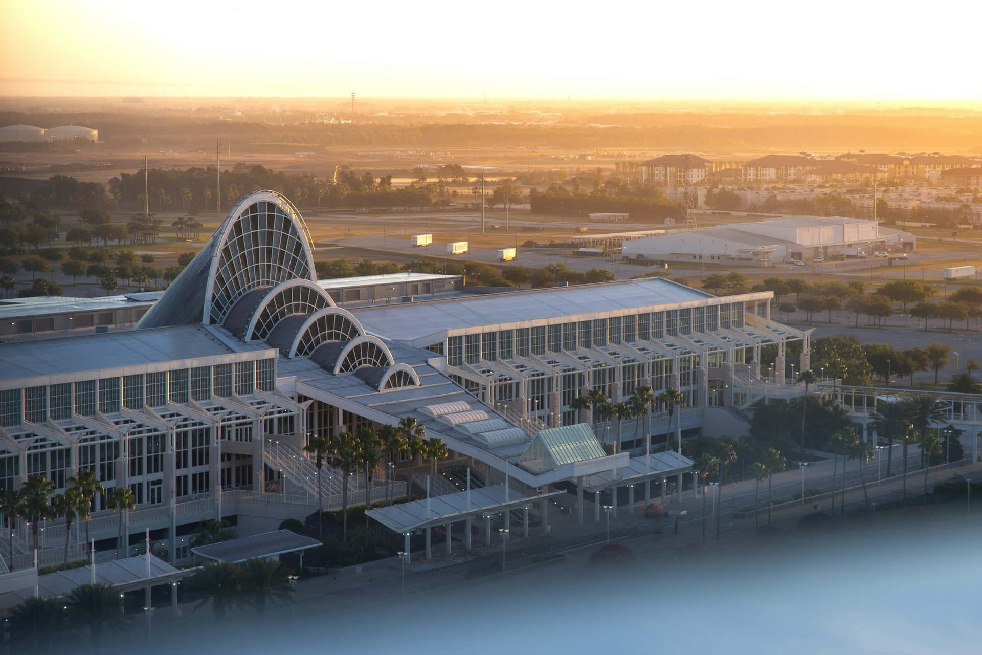 Orlando 桌布 壁紙 — 現代機場客運大樓，弧形玻璃屋頂在金色日落光芒中沐浴，俯瞰廣闊的城市景觀。
