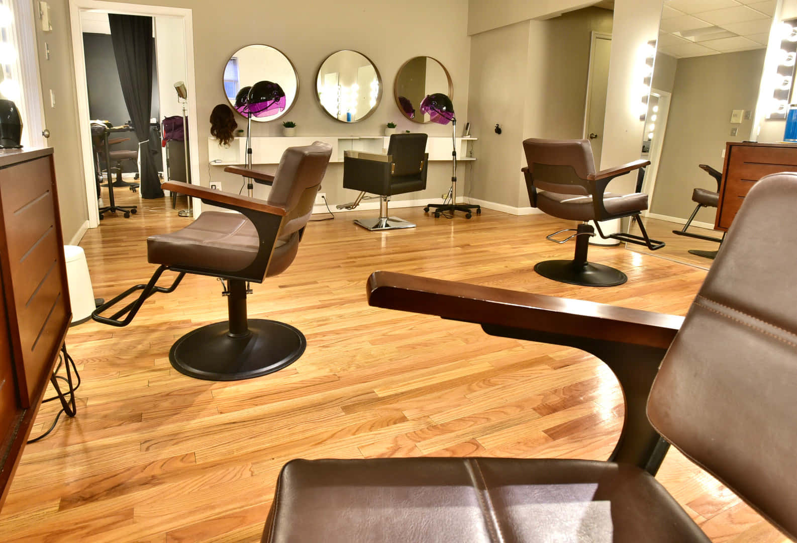 Hair Salon 桌布 壁紙 — 現代沙龍，舖有木地板，棕色皮革椅排列在圓鏡和明亮的梳妝燈下。
