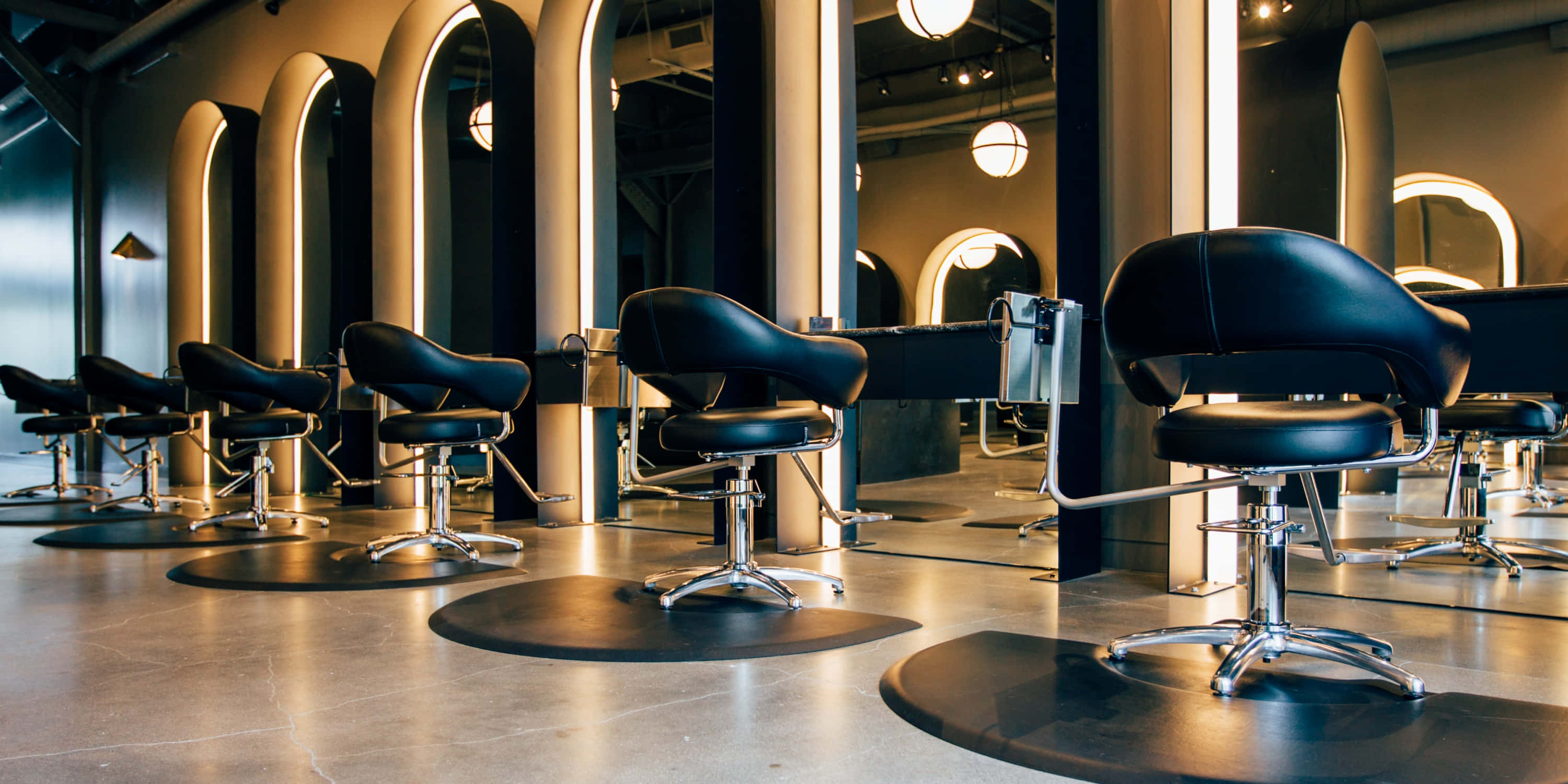 Hair Salon 桌布 壁紙 — 現代沙龍，配有黑色皮革椅子和拱形鏡子，在溫暖的燈光下閃耀。