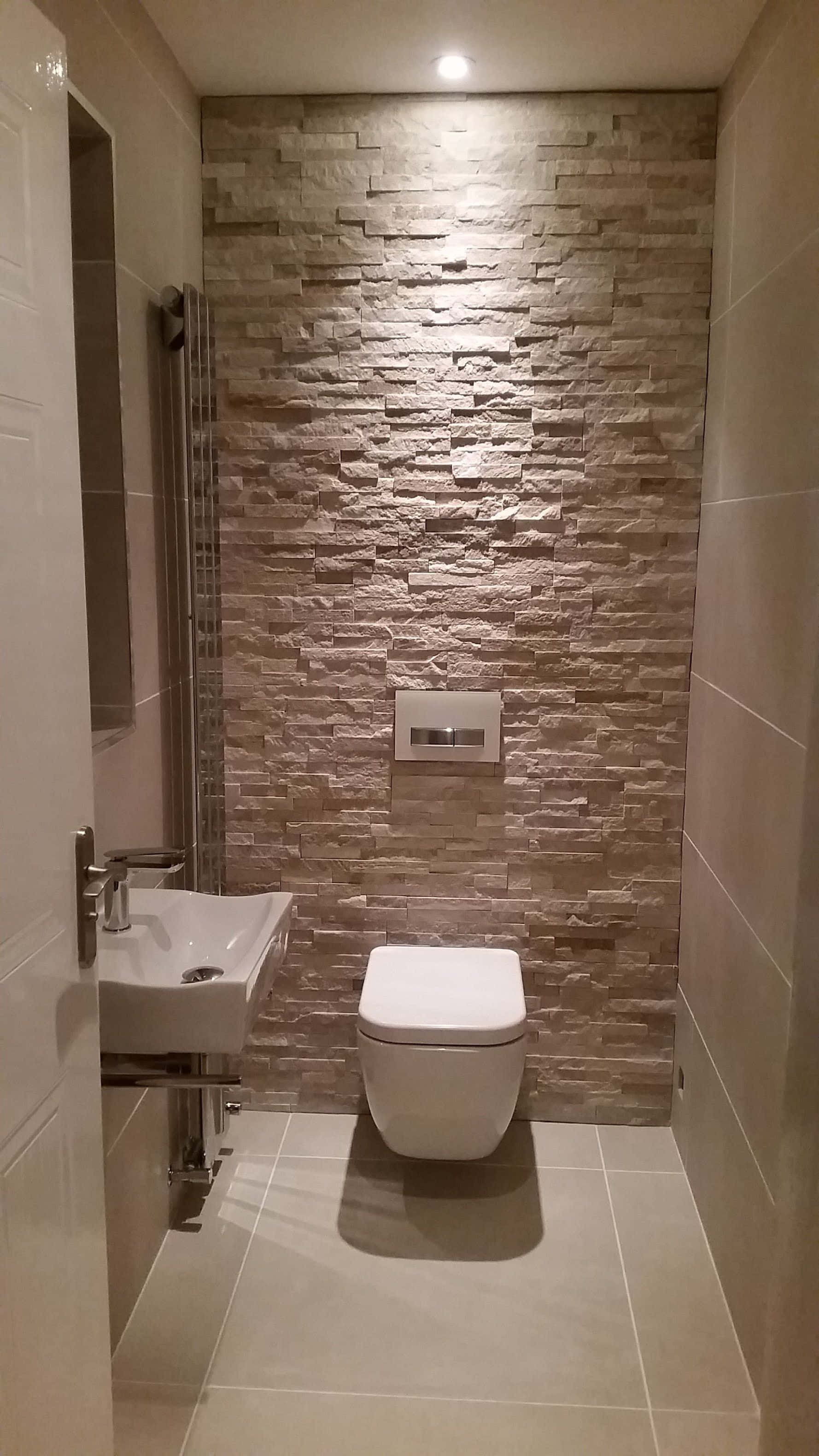 Toilet 桌布 壁紙 — 現代浴室，米色石質特色牆由天花燈照亮，上方是時尚白色馬桶和洗手盆。