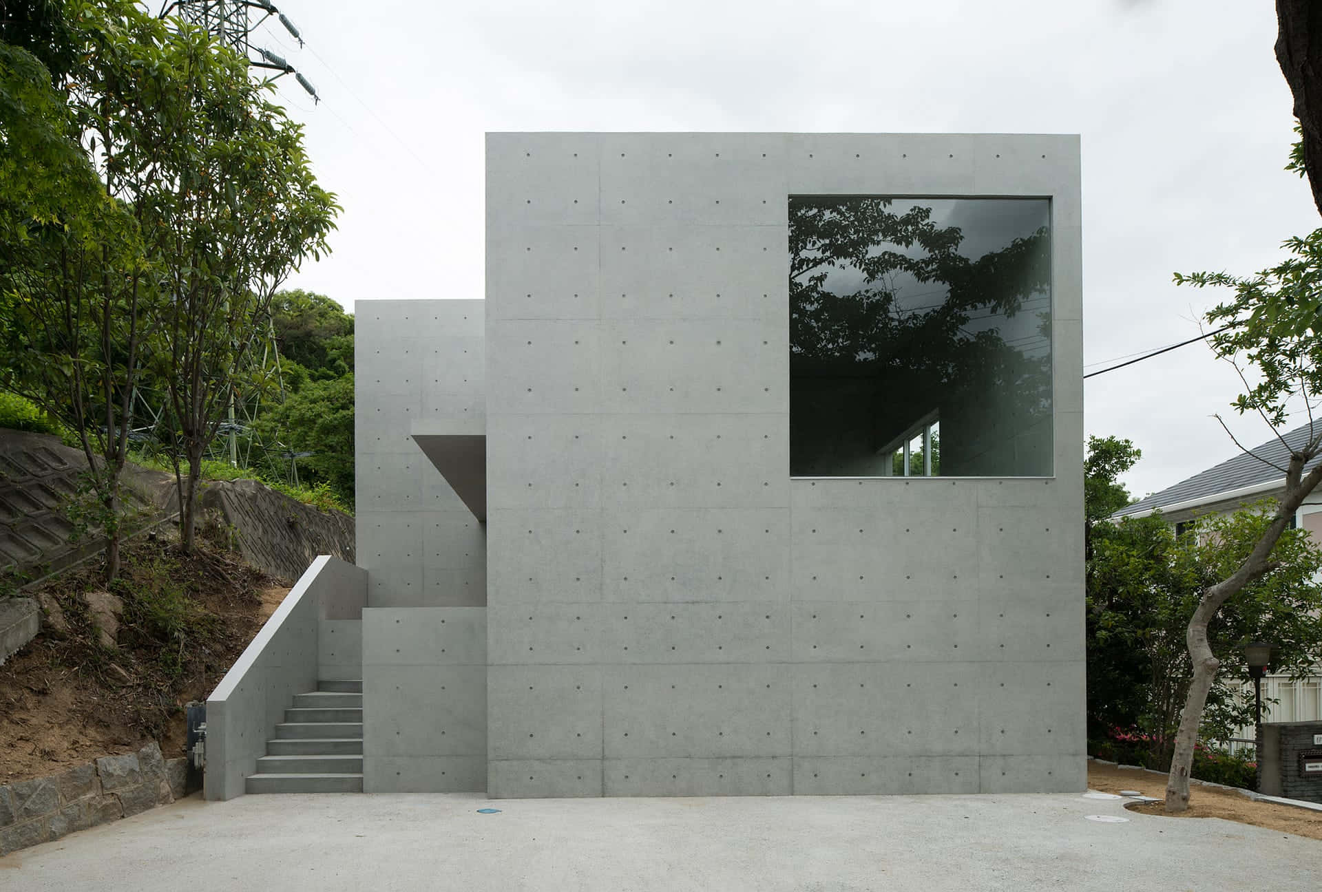 Minimalist Architecture 桌布 壁紙 — 現代混凝土建築，設有大型玻璃窗和樓梯，背景為綠樹，天空多雲。