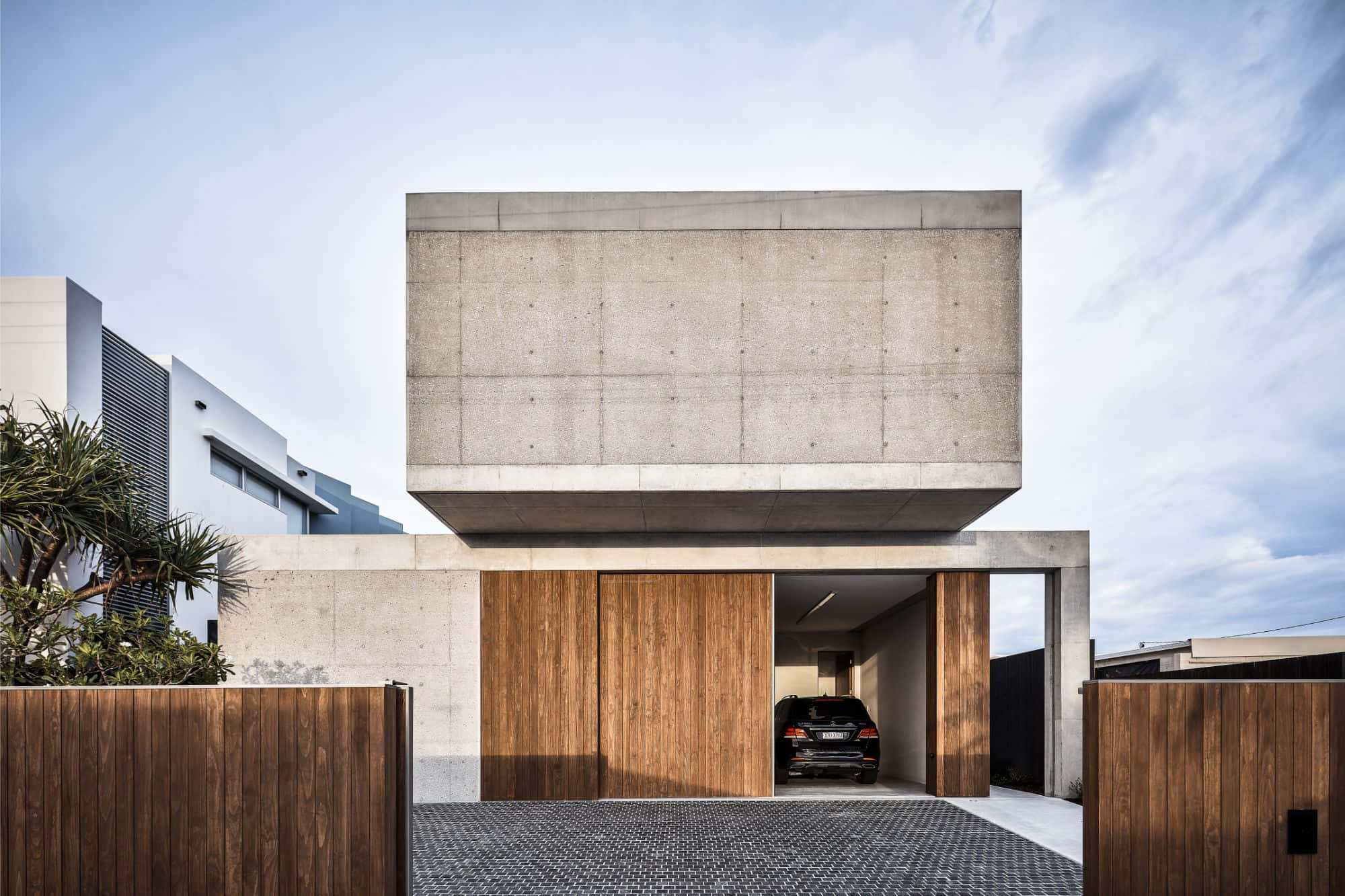 Minimalist Architecture 桌布 壁紙 — 現代混凝土房屋，配有木製車庫門和一輛停在明亮天空下的汽車。