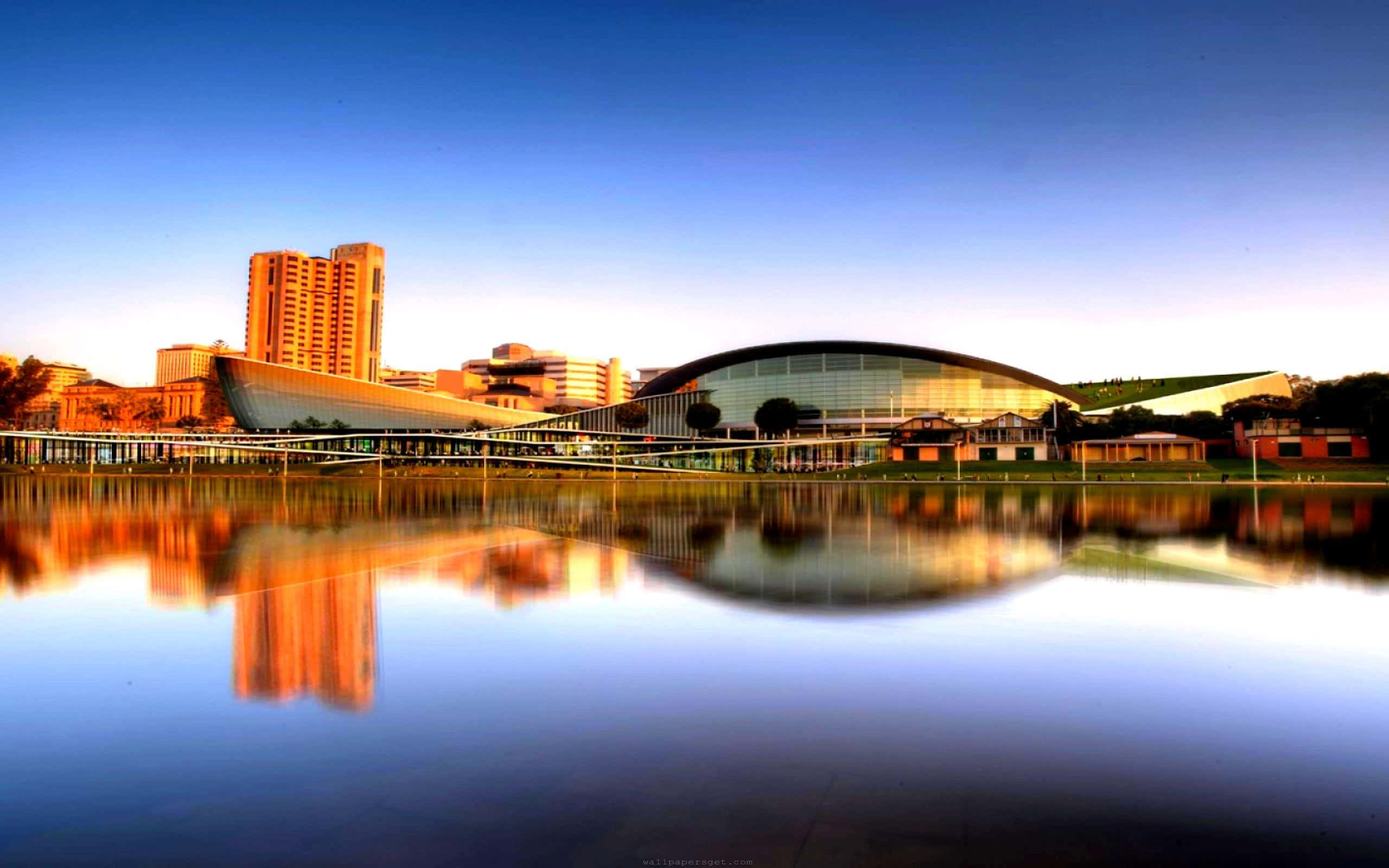 Adelaide 桌布 壁紙 — 現代玻璃圓頂建築和高塔在金色時刻倒映在平靜的水面上。
