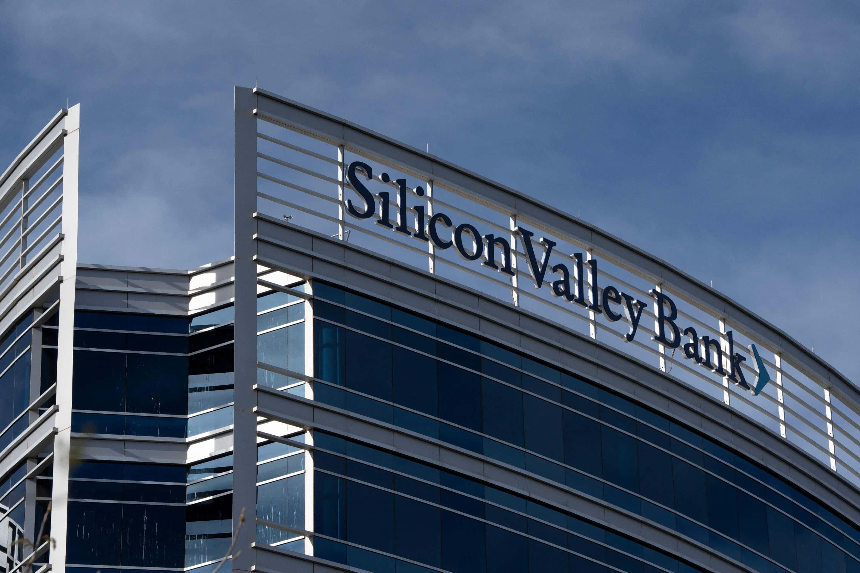 Bank 桌布 壁紙 — 現代玻璃摩天大廈，帶有「Silicon Valley Bank」標誌，背景為多雲的藍天。
