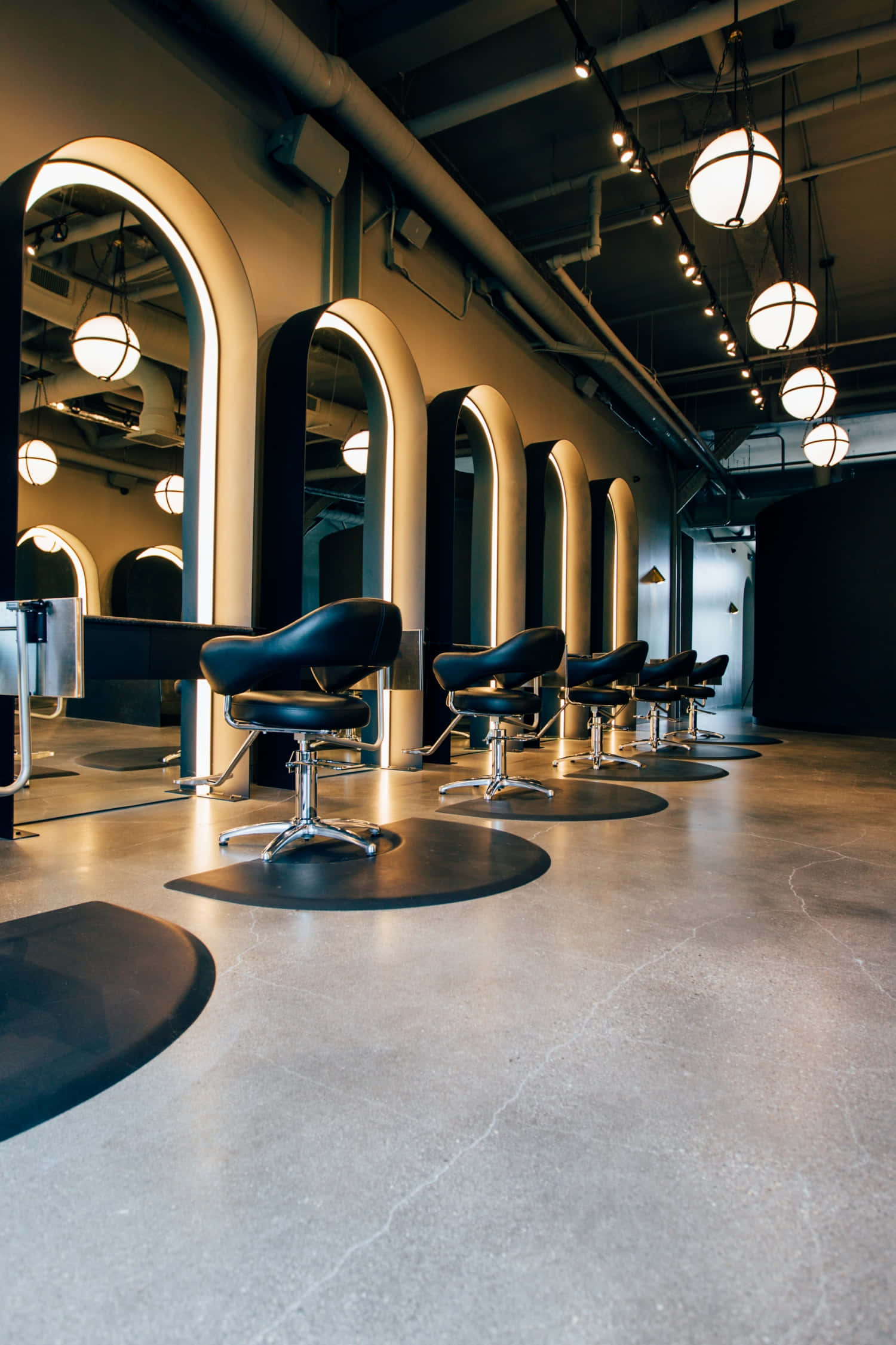 Hair Salon 桌布 壁紙 — 現代理髮店，配有時尚黑色座椅和發光的拱形鏡子，下方是工業風吊燈。