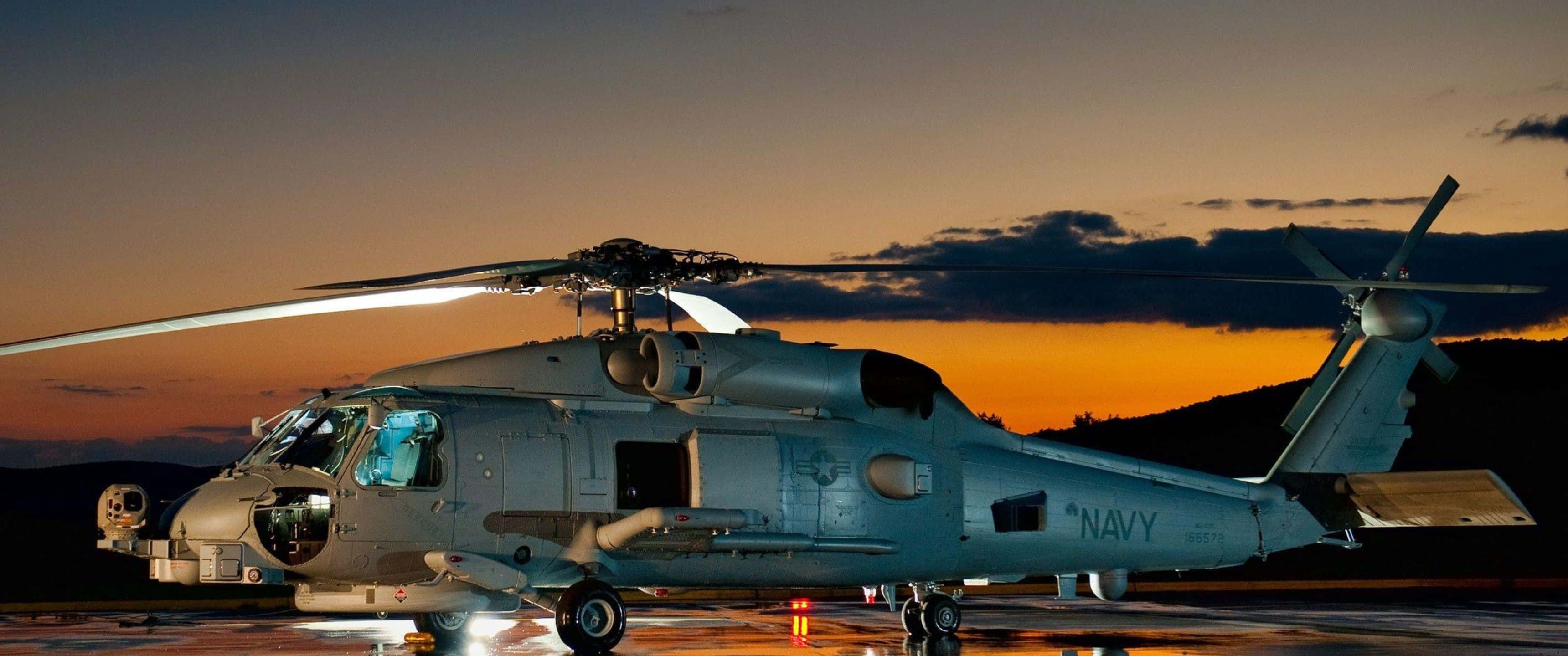 現代直升機翱翔雲端 壁紙 — 一架灰色海軍直升機停在濕滑的停機坪上，金色夕陽的光芒灑滿背後的天空。