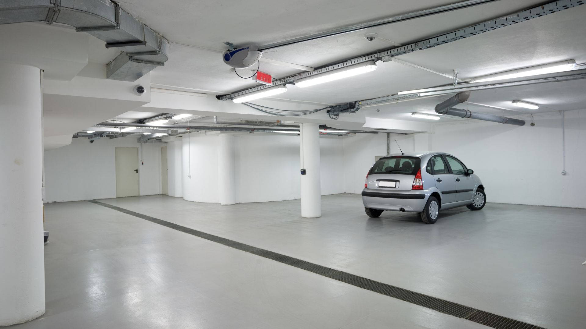 銀色汽車停放在一個乾淨空曠的地下停車場，有白色柱子和暴露的管道。