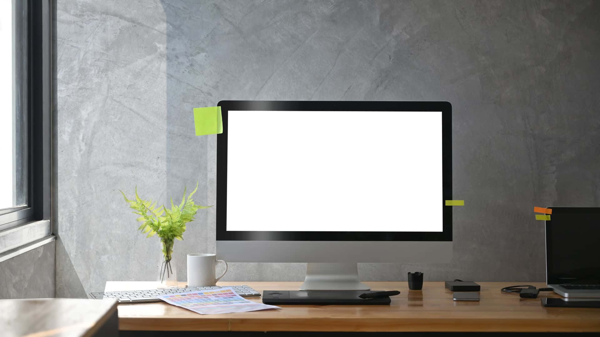Computer Screen 桌布 壁紙 — 現代簡約風格書桌，配備iMac顯示空白螢幕，旁邊窗戶有綠色植物和咖啡杯。