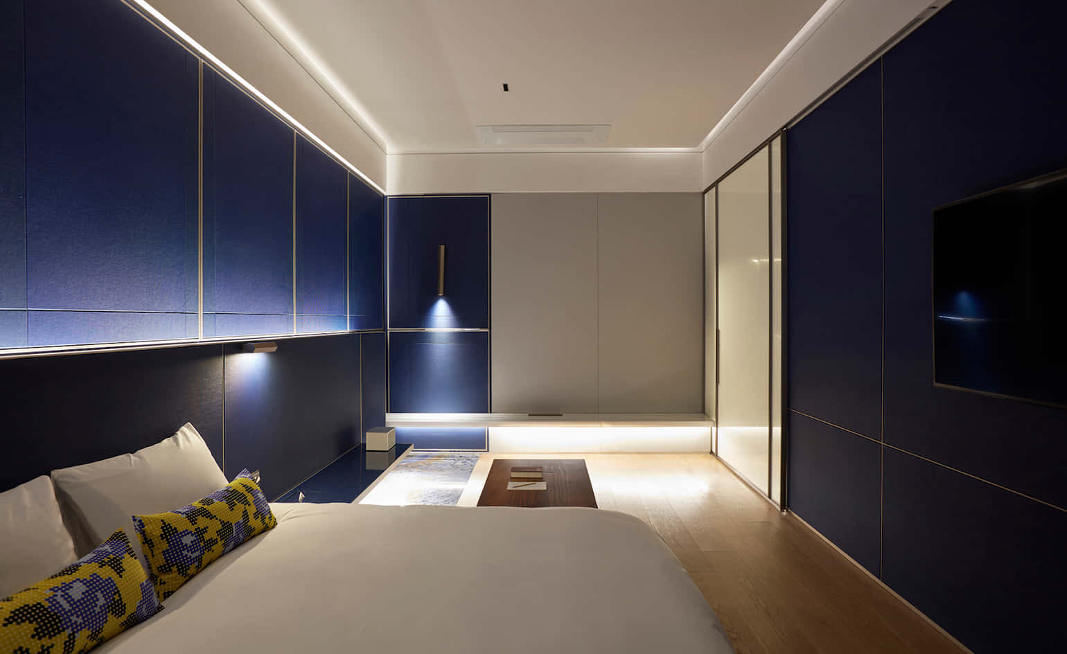 Hotel Room 桌布 壁紙 — 現代臥室，深藍色鑲板牆在環境照明下發光，配以木地板。