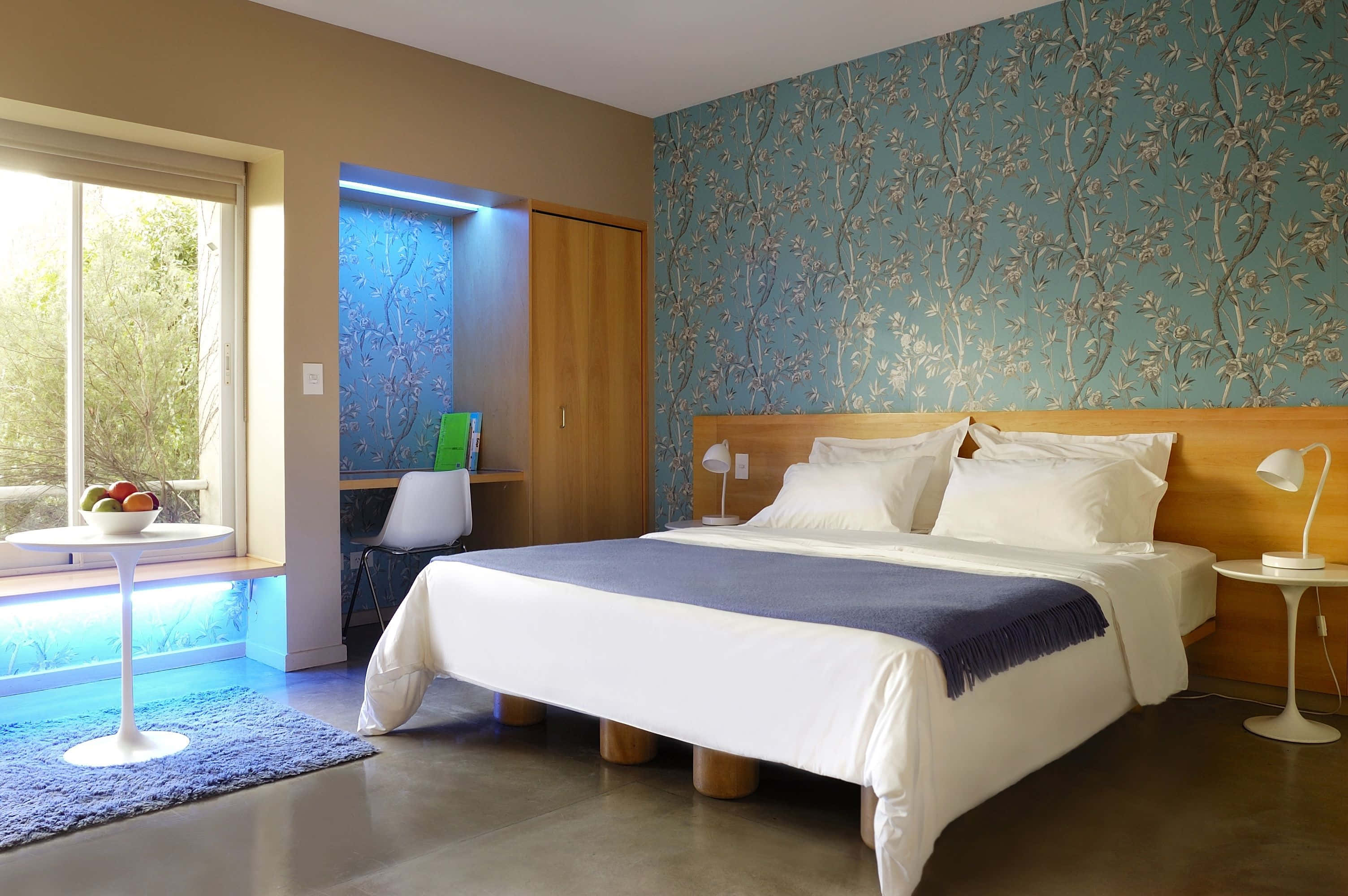 Hotel Room 桌布 壁紙 — 現代臥室，配有木床、藍色花卉壁紙，以及可俯瞰綠意的窗戶，搭配藍色環境照明。