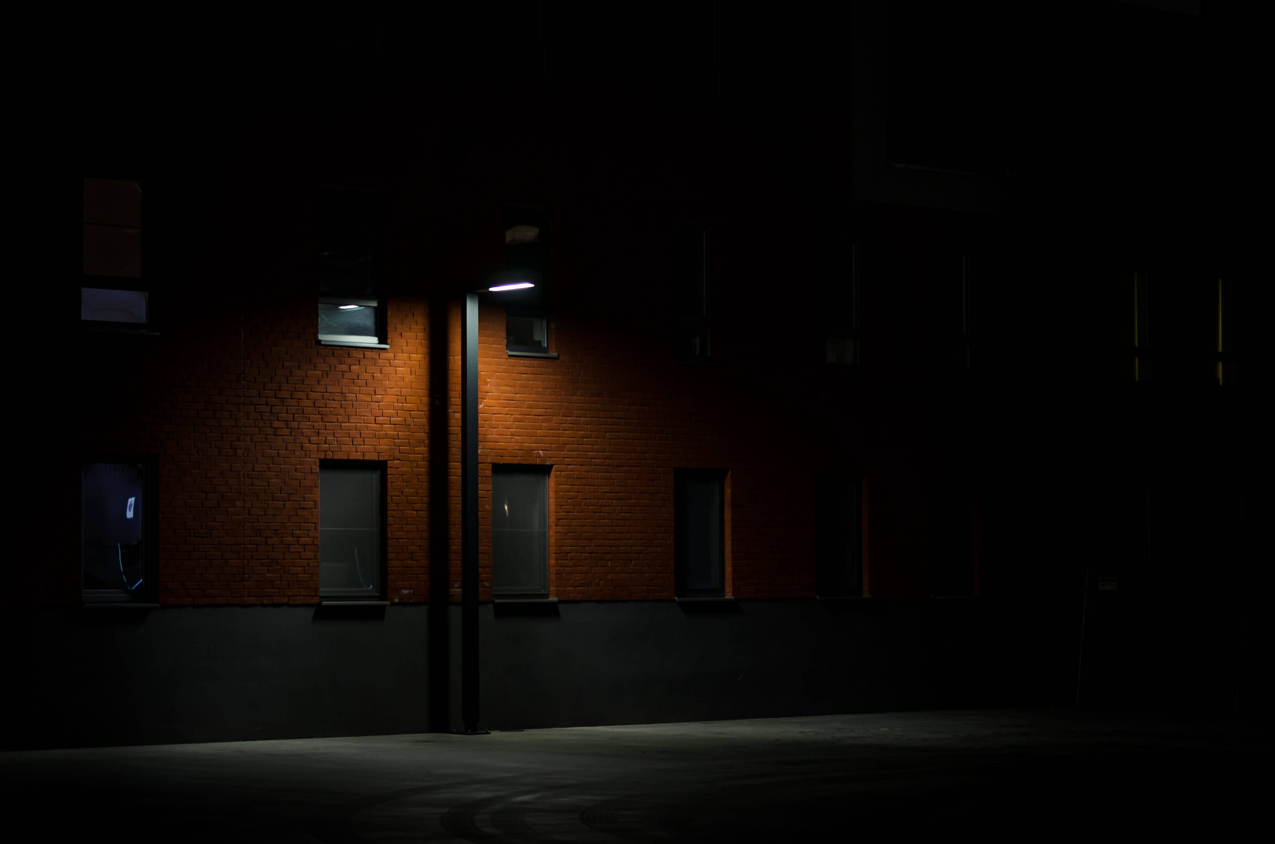 現代街燈暗調4K 壁紙 — 一盞路燈在夜間將溫暖的光線投射在磚砌建築的外牆上，照亮了幾扇窗戶，與深沉的陰影形成對比。
