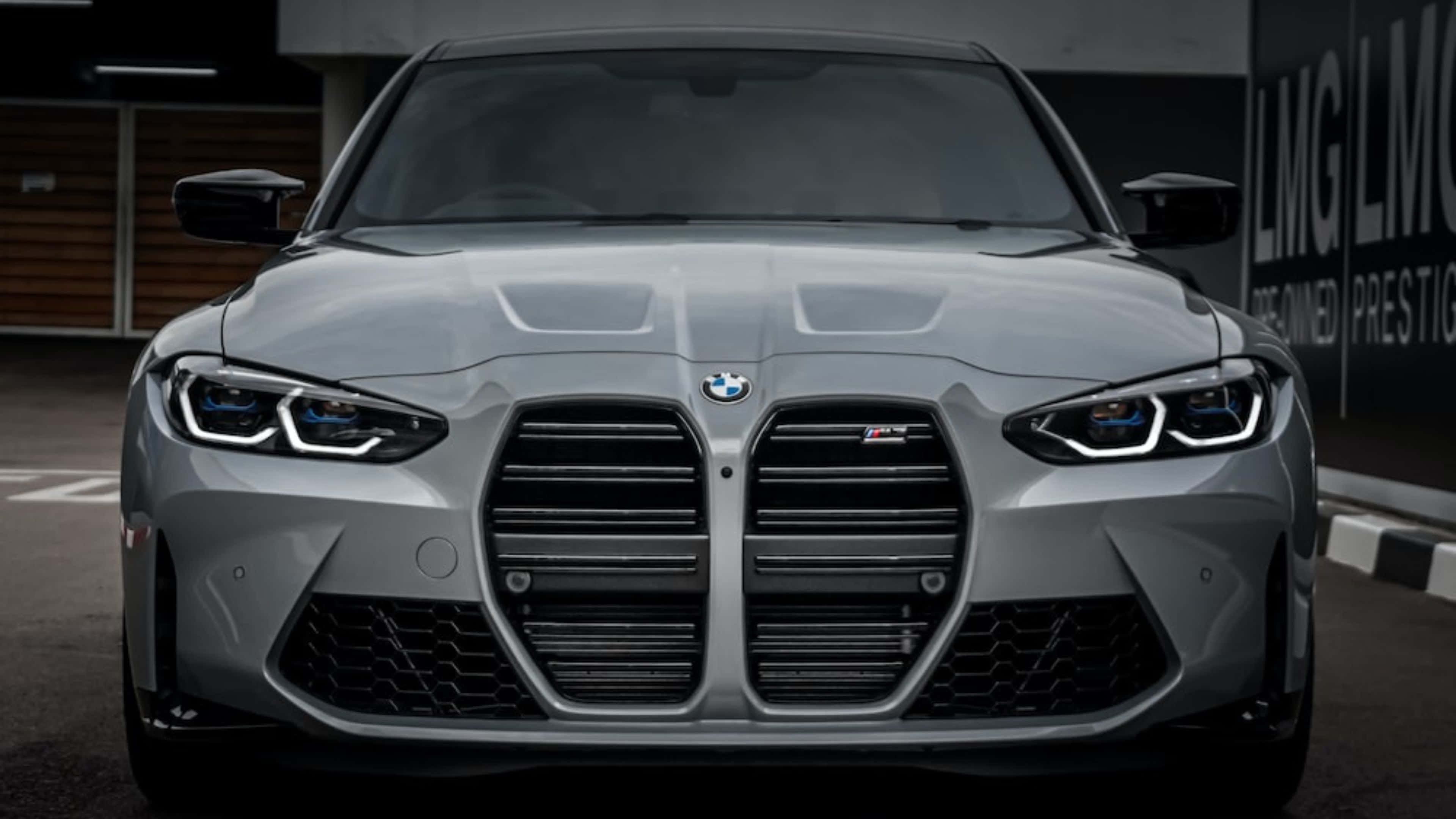 4K BMW 壁紙 桌布 壁紙 — 現代車庫中停放的銀色寶馬M3前視圖，配備激進格柵和發光頭燈。