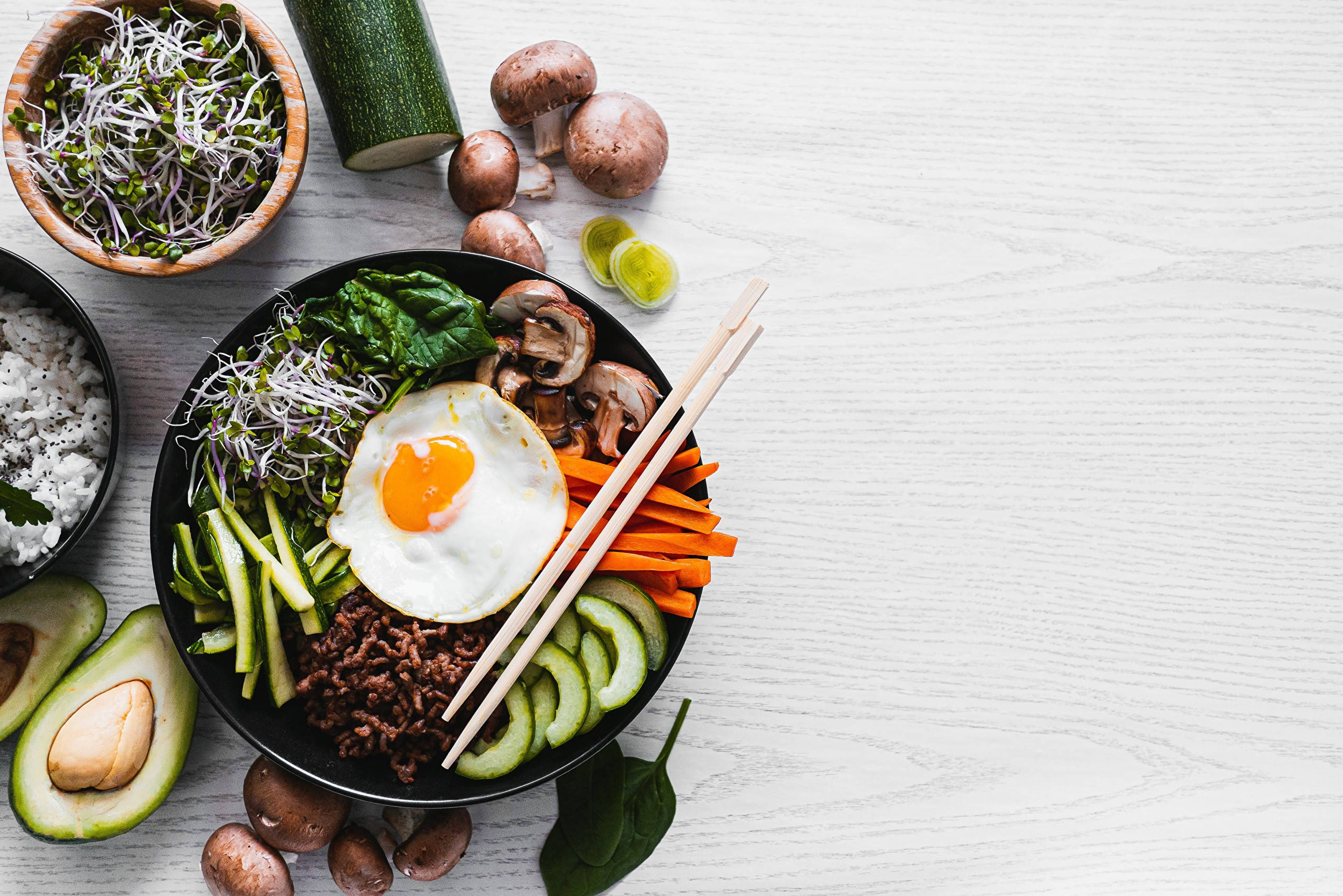 現代風味拌飯 壁紙 — 一張充滿活力的俯拍照片，展示色彩繽紛的韓國石鍋拌飯，上面有太陽蛋和新鮮蔬菜，放在白色木質表面上。