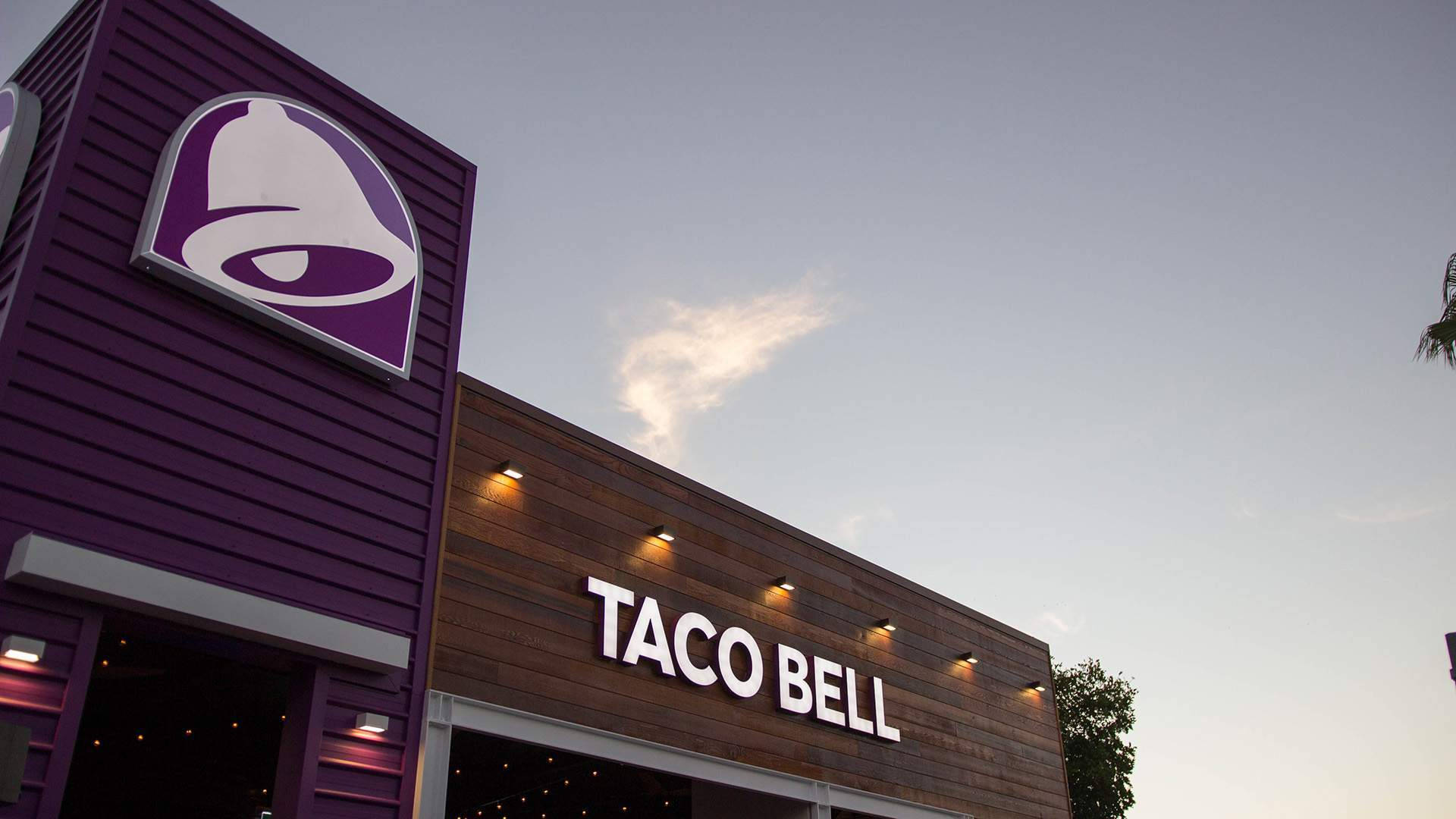 現代風格Taco Bell分店 壁紙 — 黃昏時分的Taco Bell餐廳，紫色牆板和發光招牌映襯著柔和天空。