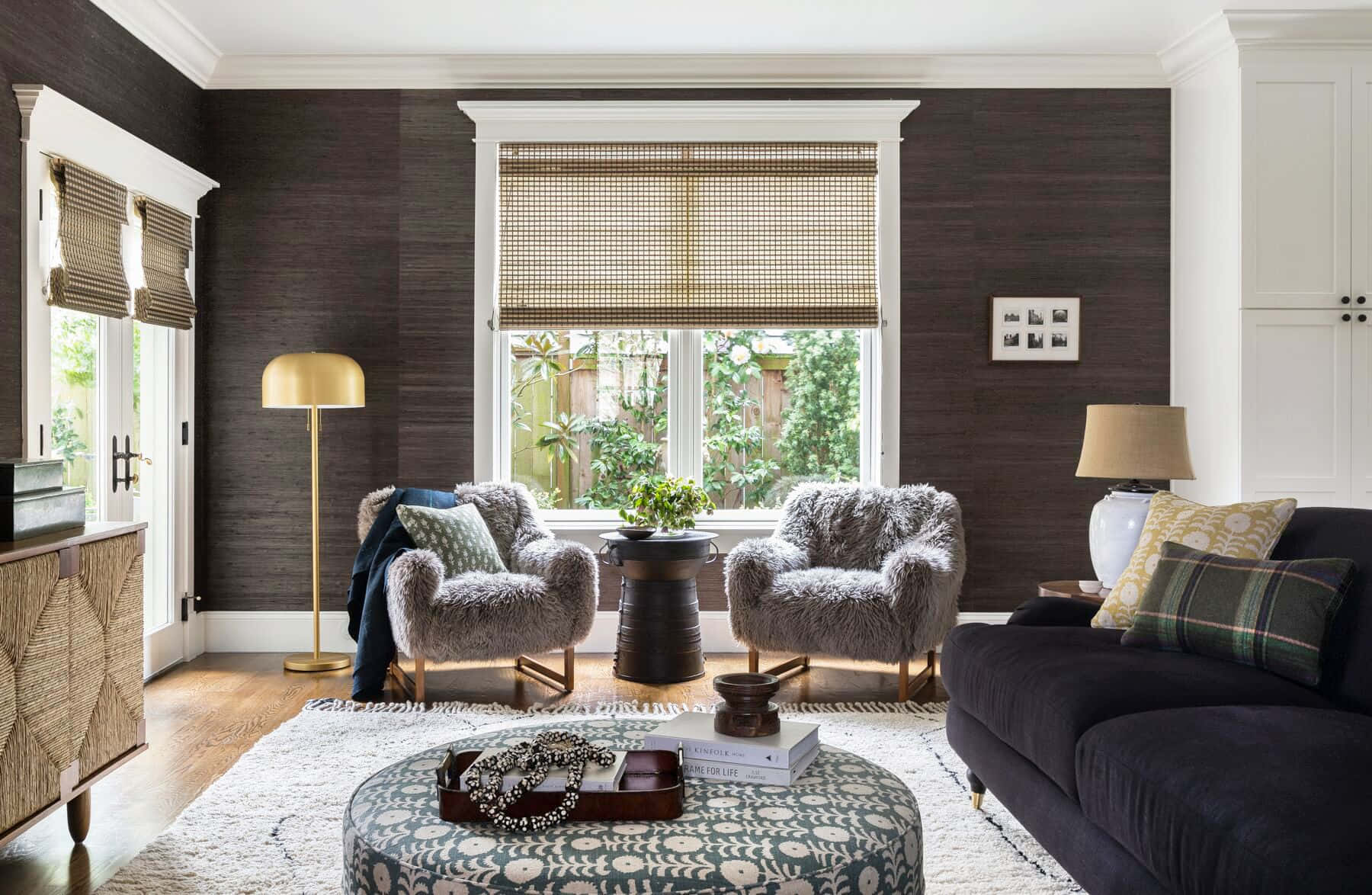 現代風格客廳住宅內裝 壁紙 — 一個舒適的客廳，設有深色木鑲板牆壁、蓬鬆的灰色椅子，以及一個在溫暖金色燈光下的圖案軟凳。