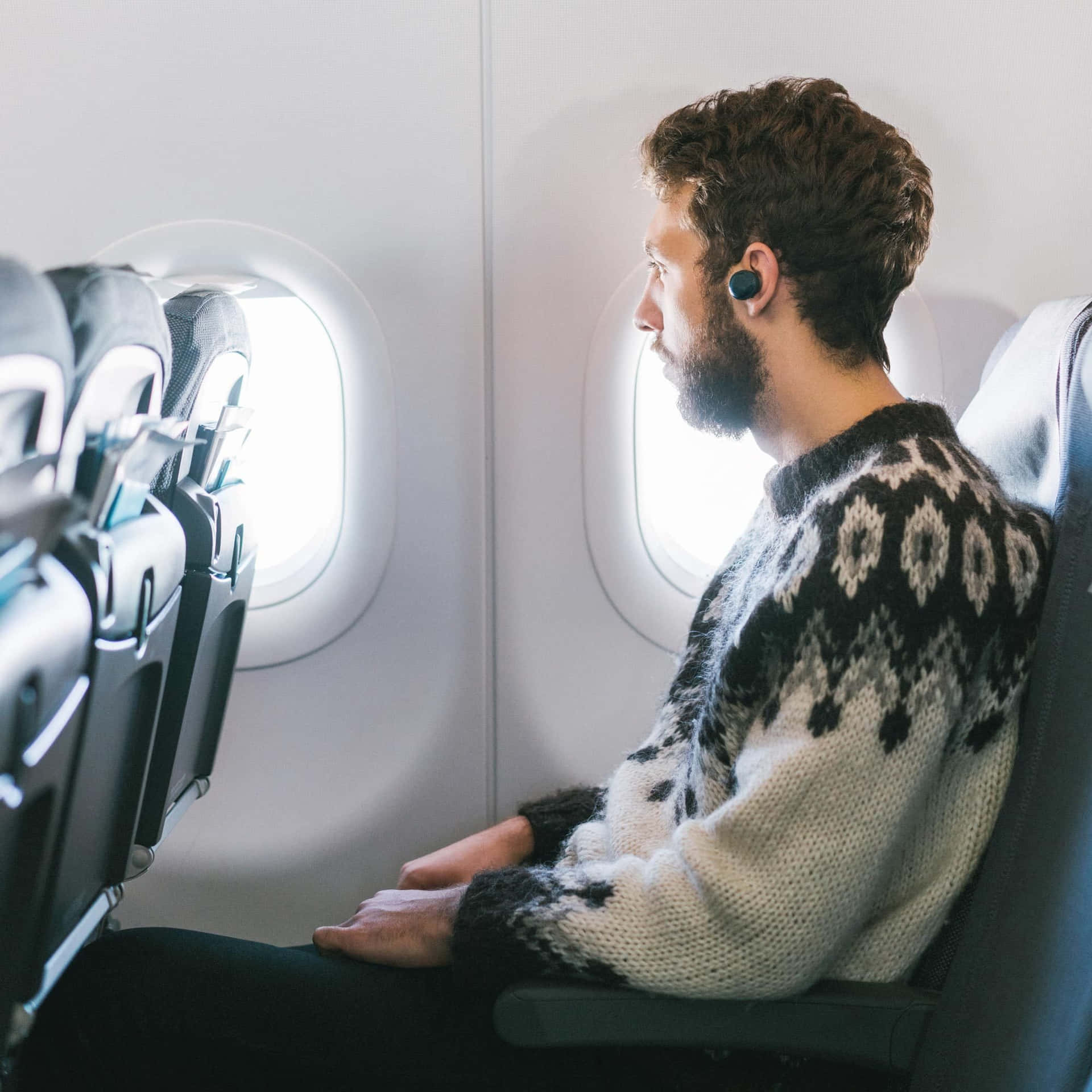 穿圖案毛衣的男士戴著耳機望向飛機窗外