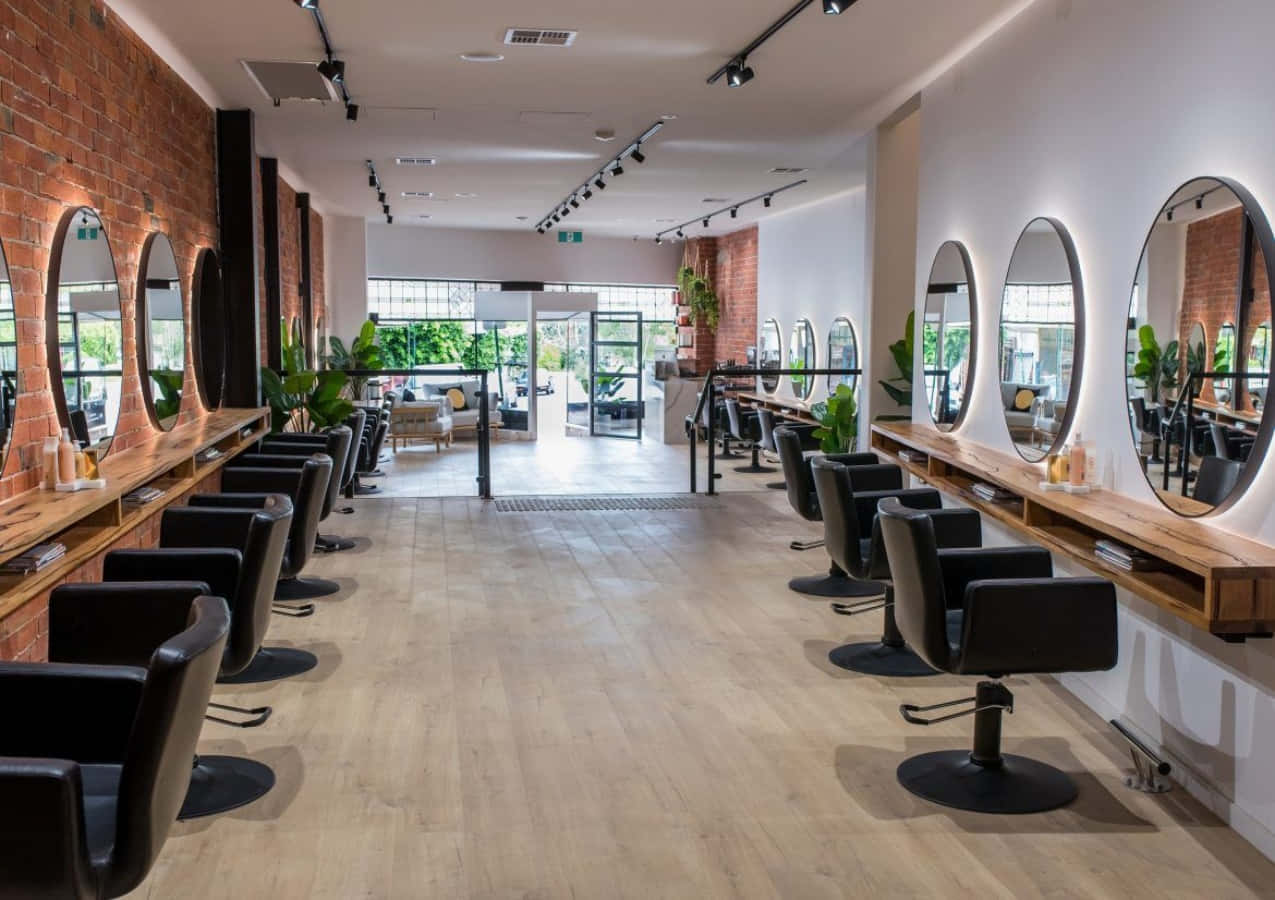 Hair Salon 桌布 壁紙 — 現代髮廊，暖色燈光下排列著黑色椅子與圓形鏡子，背景為裸露磚牆。
