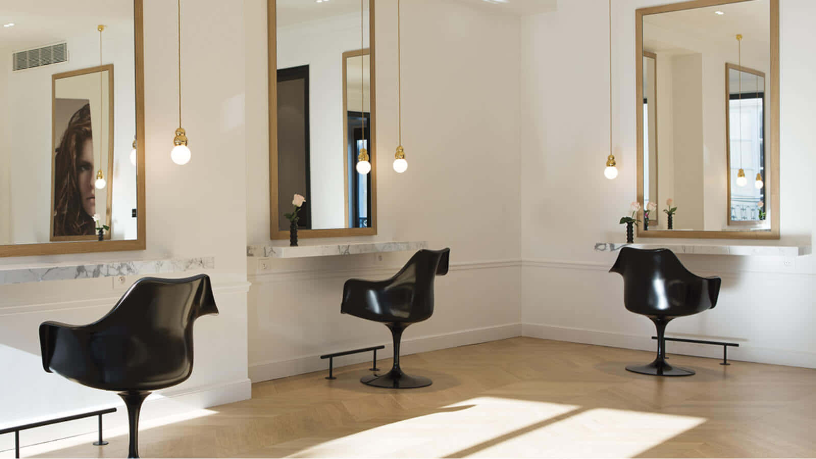 Hair Salon 桌布 壁紙 — 現代髮廊，配有黑色椅子、大理石檯面和大型鏡子，反射溫暖的吊燈和陽光在魚骨紋木地板上。