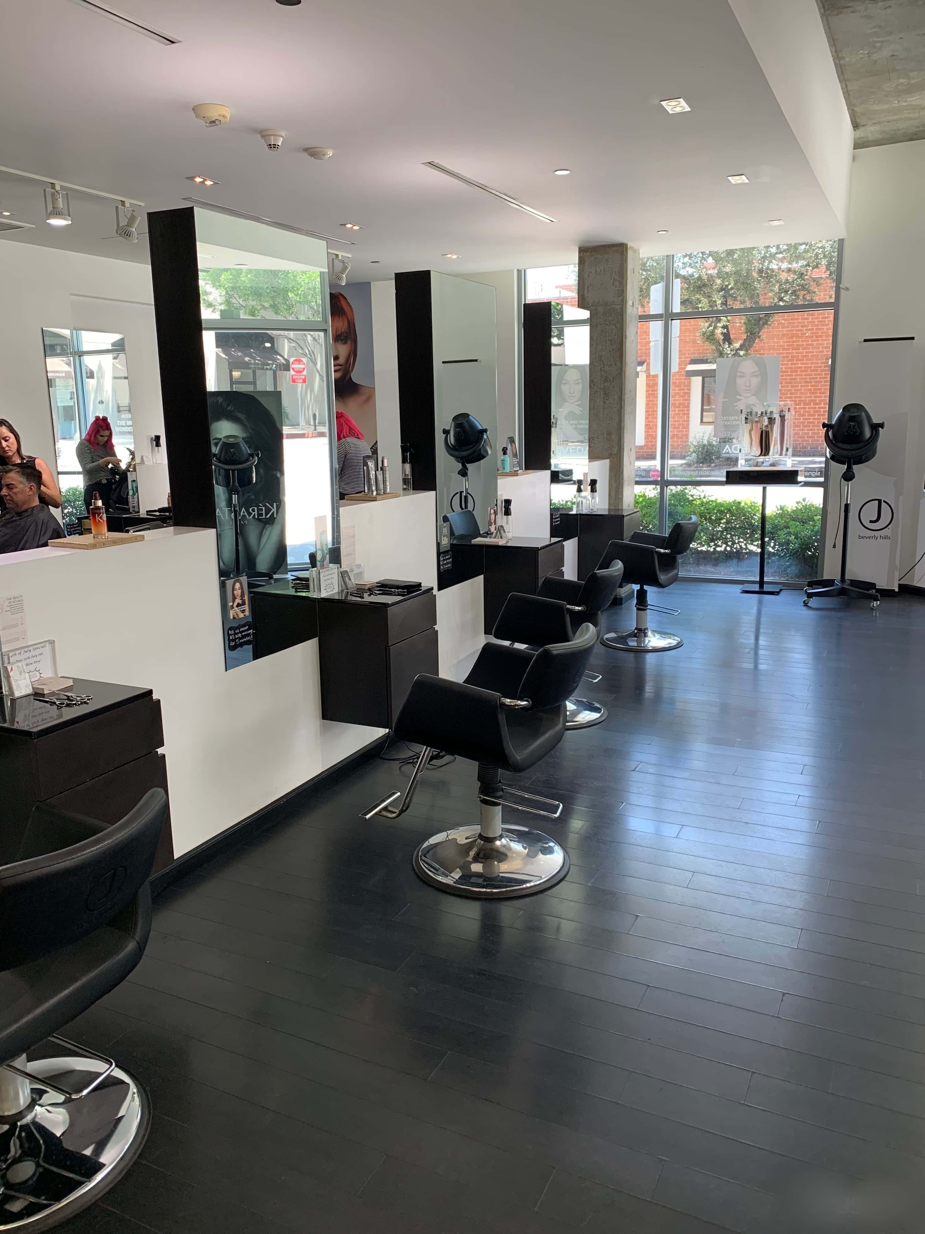 Hair Salon 桌布 壁紙 — 現代髮廊，配有黑色椅子和鏡子，透過大窗戶反射明亮的日光。
